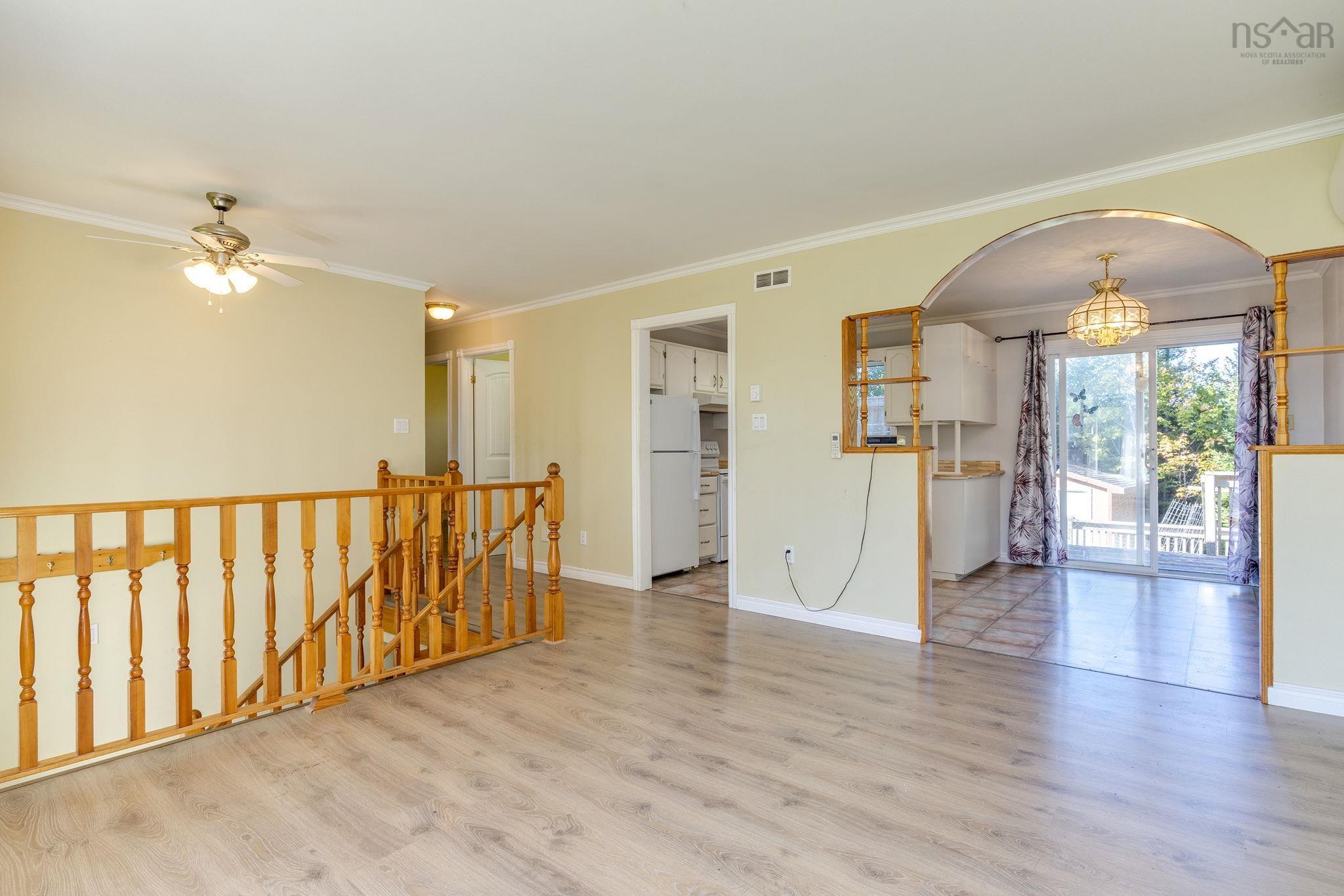 128 Doherty Drive, Lawrencetown, NS (MLS® 202625891) — Open-concept interior featuring light wood-finish flooring, a decorative arched wall opening, wood banister railing, and a sliding glass door