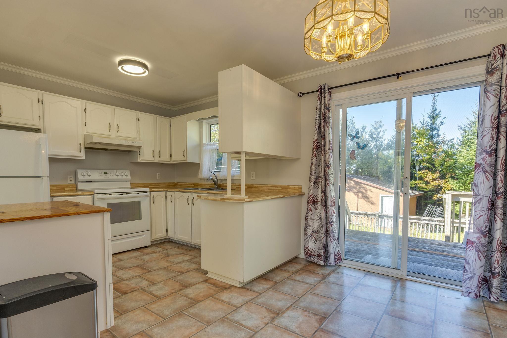 128 Doherty Drive, Lawrencetown, NS (MLS® 202625891) — Kitchen featuring white cabinetry, wood-finish countertops, ceramic tile flooring, a multi-tiered pendant light fixture, and sliding glass doors