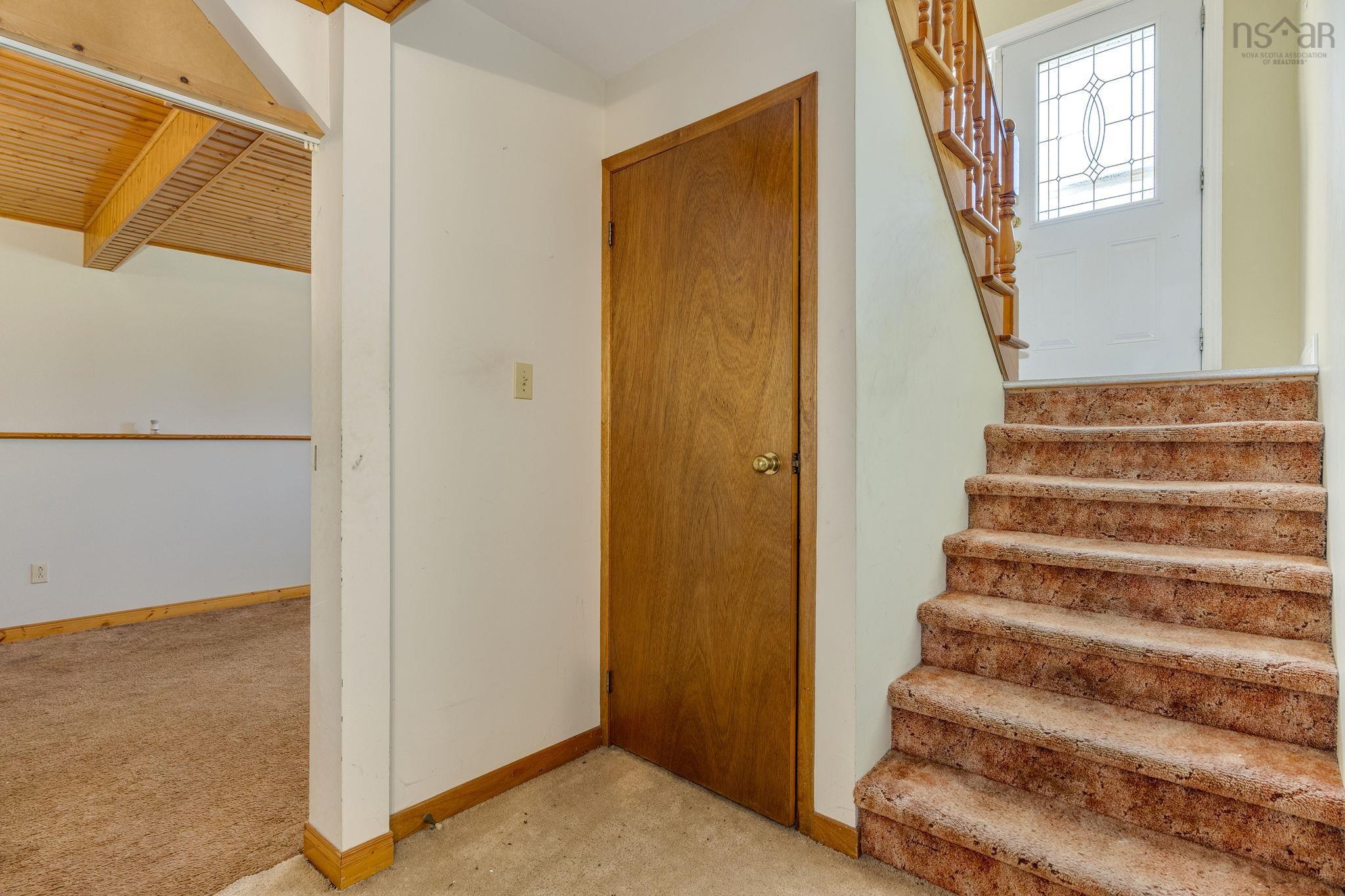 128 Doherty Drive, Lawrencetown, NS (MLS® 202625891) — Interior entryway featuring wood-tone trim, a solid-core interior door, carpeted staircase with decorative wooden railing, and an exterior door with a multi-pane glass insert