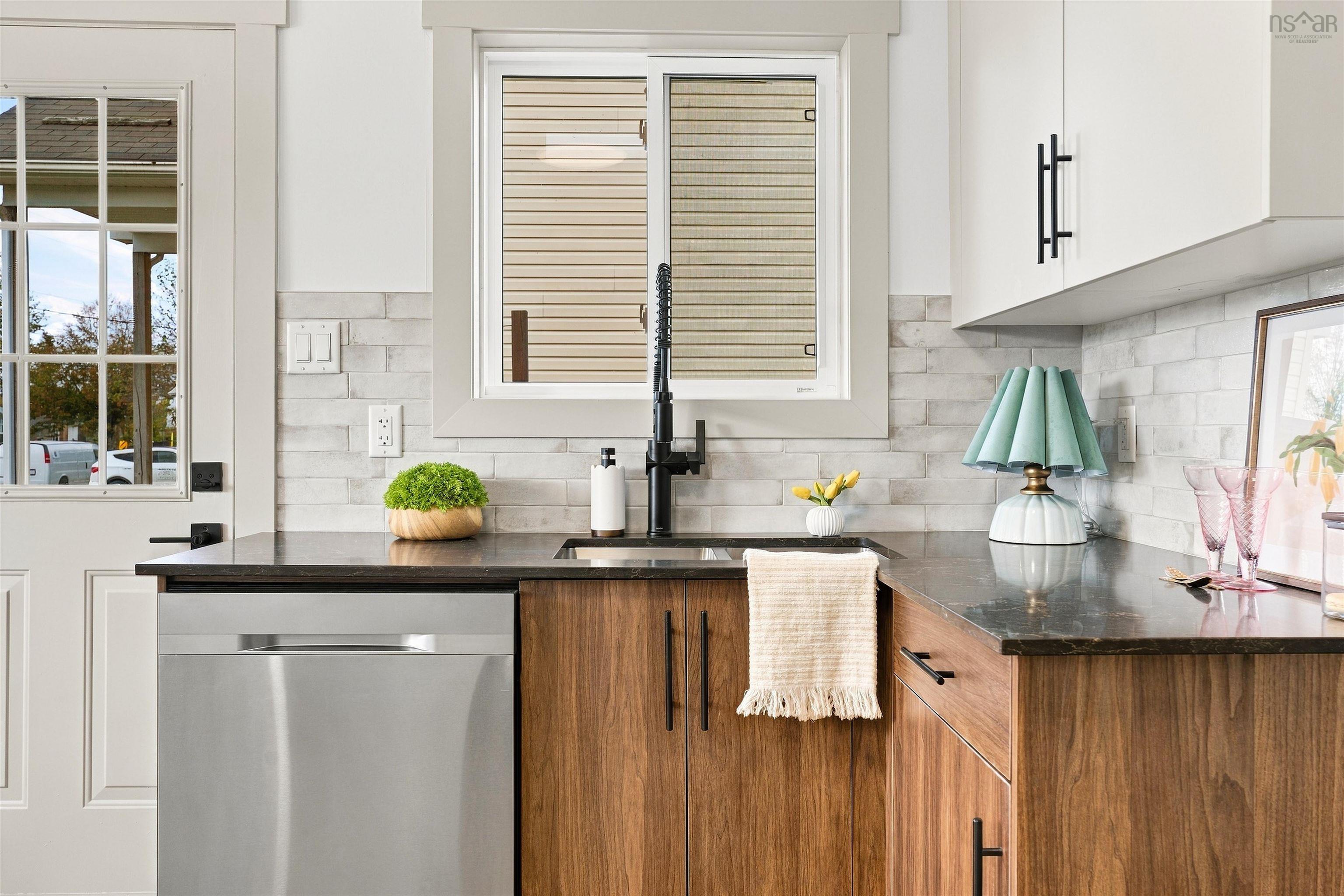 74 1/2 Belle Vista Drive, Dartmouth, NS (MLS® 202625912) — Kitchen workspace featuring dark stone countertops, wood-finish cabinetry, matte black hardware, a high-arc faucet, and a light-toned brick-style backsplash
