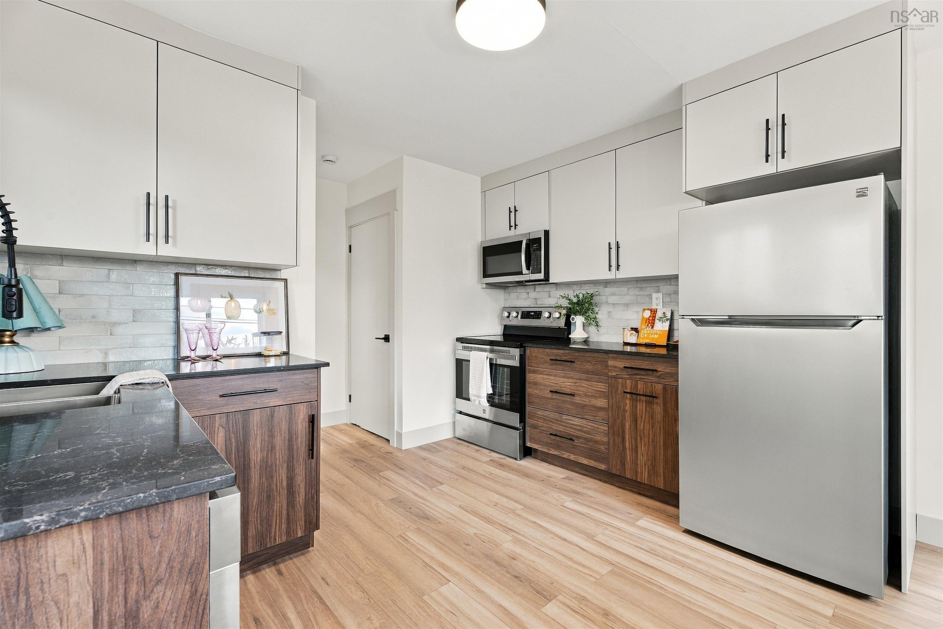 74 1/2 Belle Vista Drive, Dartmouth, NS (MLS® 202625912) — Kitchen featuring two-tone cabinetry with wood-finish lower units and matte white upper units, stone-surface countertops, horizontal tile backsplash, stainless steel appliances, and wood-finish flooring