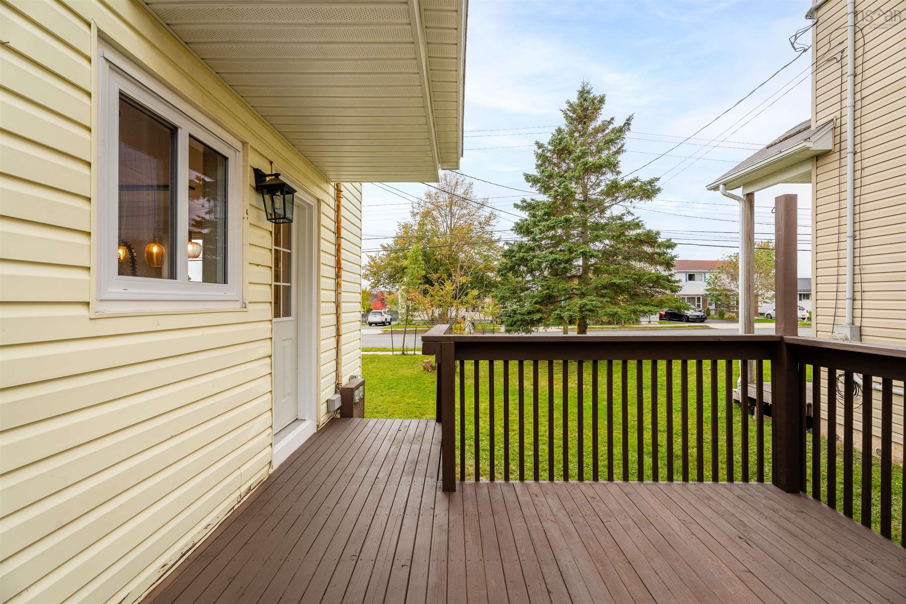 74 1/2 Belle Vista Drive, Dartmouth, NS (MLS® 202625912) — Exterior deck with dark-stained wood decking and matching vertical railings, light-colored horizontal siding, and a wall-mounted outdoor lantern fixture