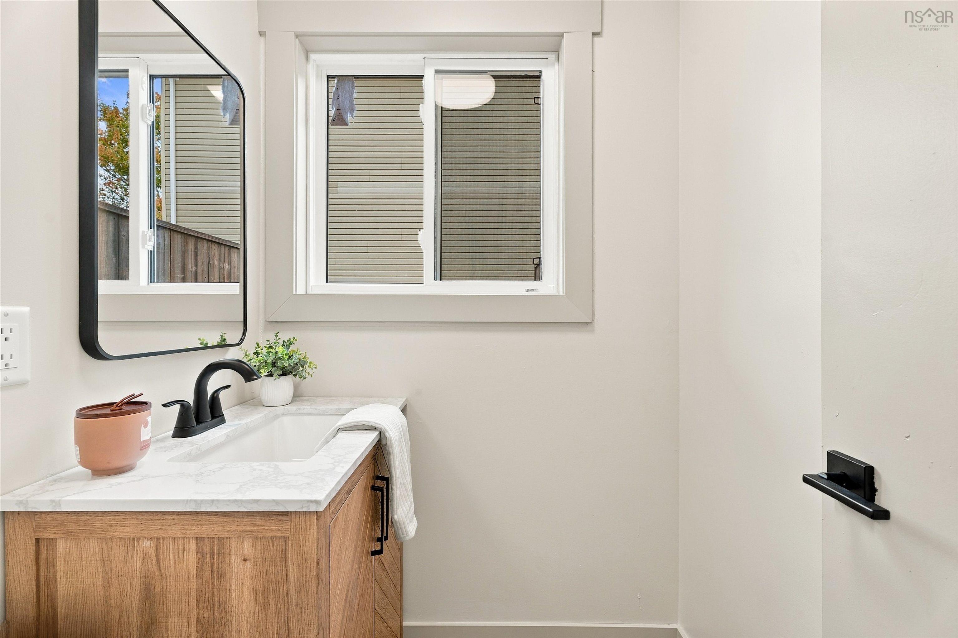74 1/2 Belle Vista Drive, Dartmouth, NS (MLS® 202625912) — Wood-finish cabinetry vanity with stone-look countertop, integrated rectangular sink, matte black faucet, and matching framed mirror
