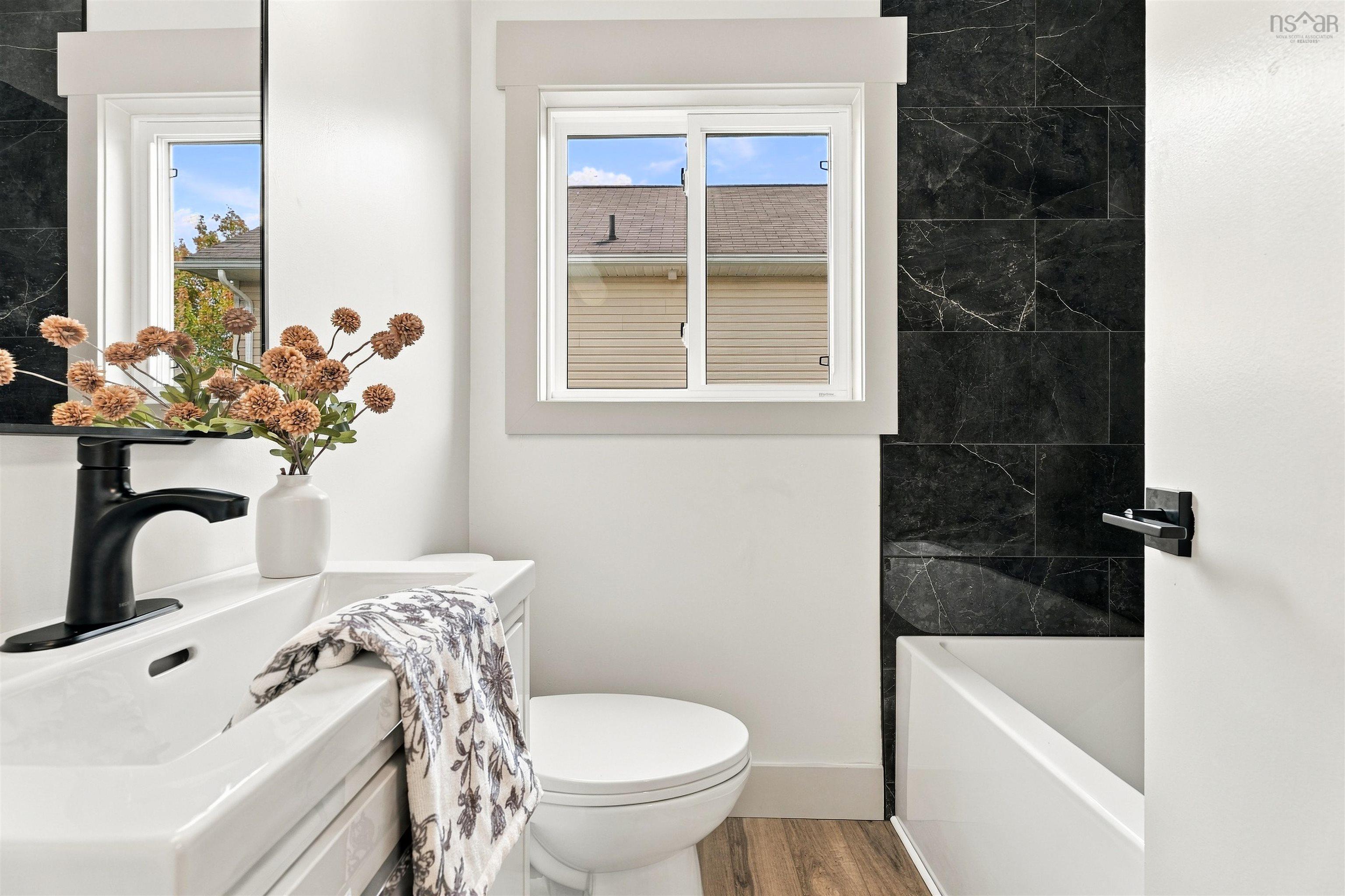 74 1/2 Belle Vista Drive, Dartmouth, NS (MLS® 202625912) — Bathroom featuring a vanity with integrated sink, matte black faucet, wood-finish flooring, and a tub surround with dark, large-format tile