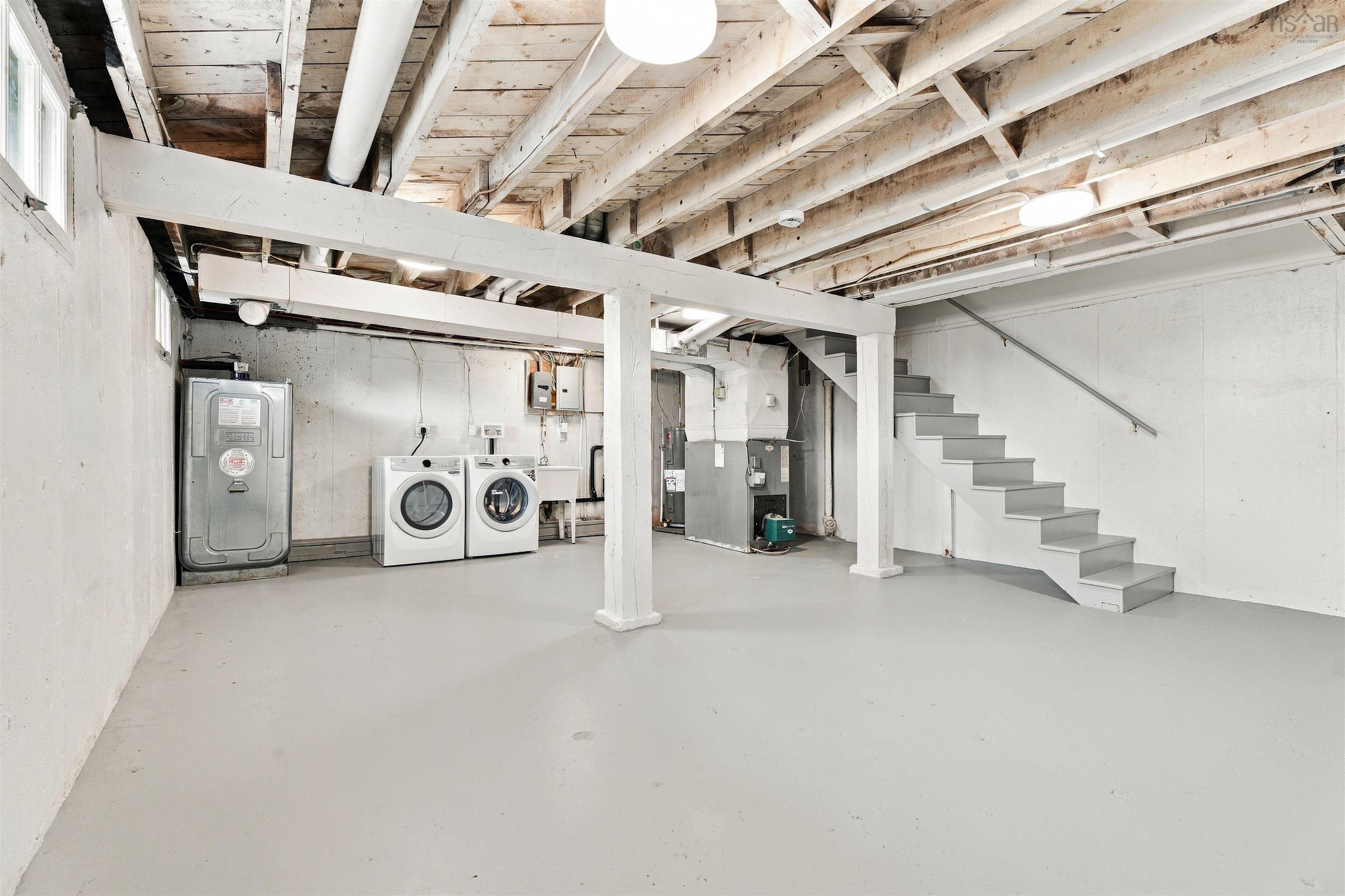 74 1/2 Belle Vista Drive, Dartmouth, NS (MLS® 202625912) — Unfinished lower level featuring painted concrete flooring, exposed timber ceiling joists, a built-in utility sink, and a staircase with a handrail