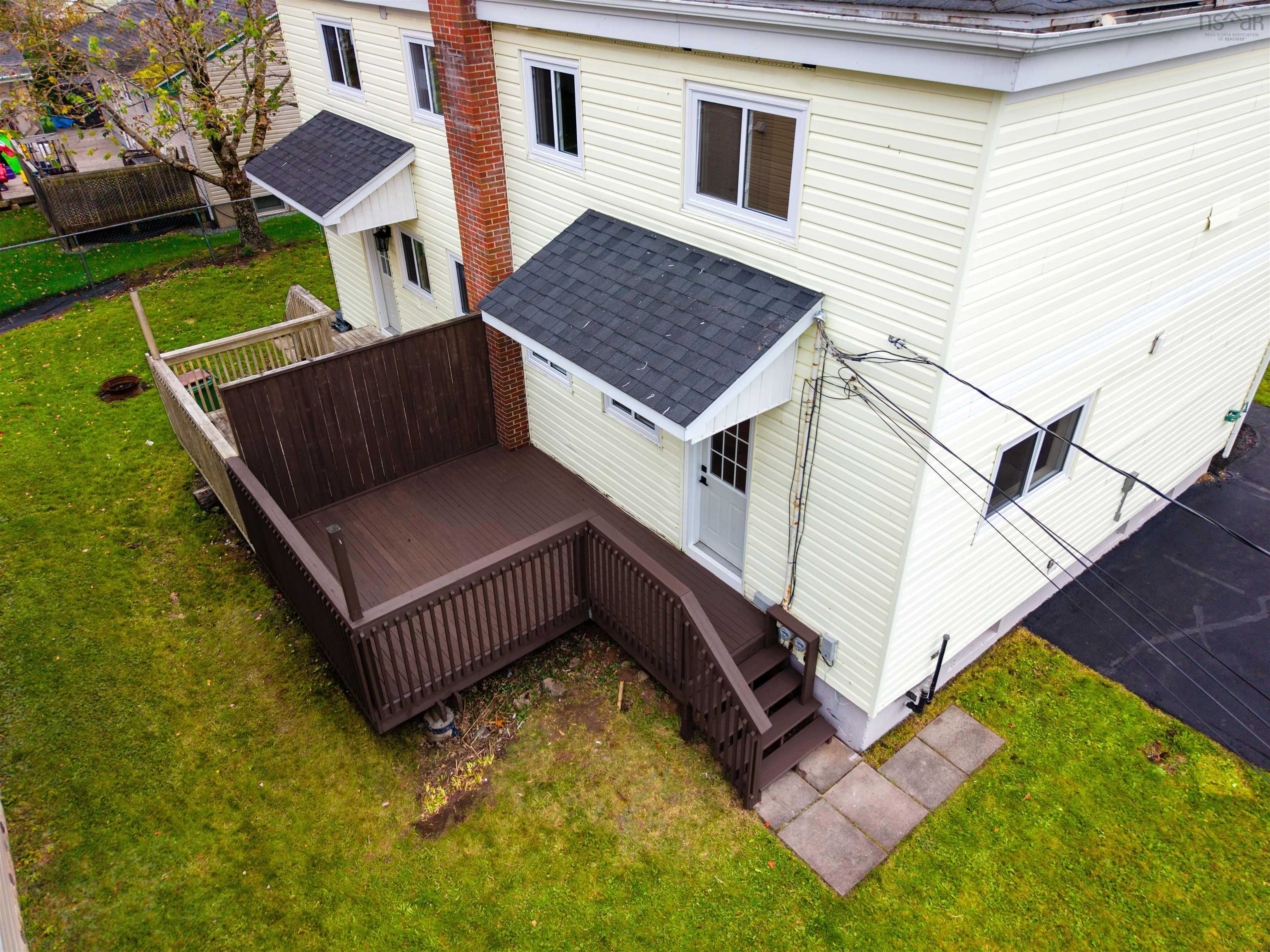 74 1/2 Belle Vista Drive, Dartmouth, NS (MLS® 202625912) — Exterior featuring cream-colored siding, a dark-toned wood deck with matching balustrades, an exposed red-brick chimney, and asphalt shingle roof accents