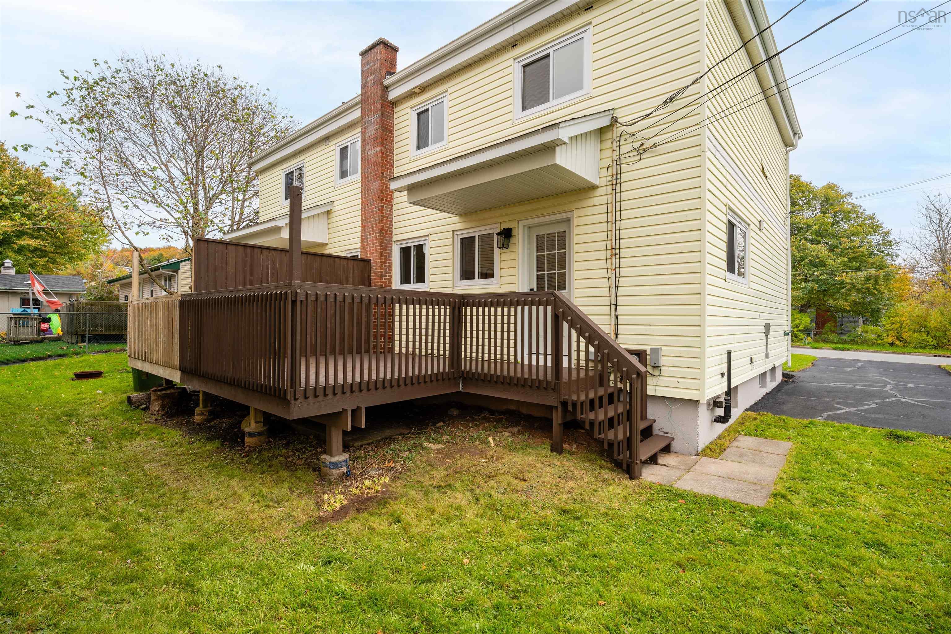 74 1/2 Belle Vista Drive, Dartmouth, NS (MLS® 202625912) — Exterior featuring light-toned horizontal siding, a raised wood deck with balustrades, a prominent exterior masonry chimney, and a paved driveway