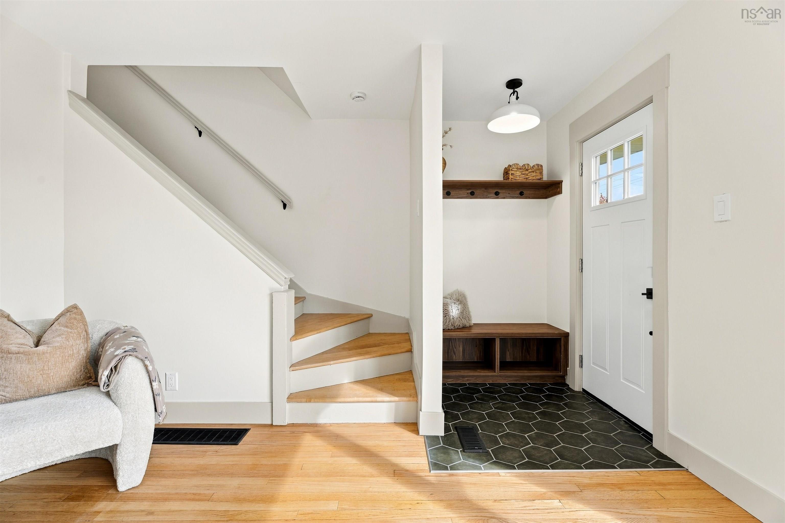 74 1/2 Belle Vista Drive, Dartmouth, NS (MLS® 202625912) — Entryway featuring hexagonal tile flooring, built-in wooden bench and shelving, wood-finish flooring, a white paneled door with glass detail, and a wood-railed staircase