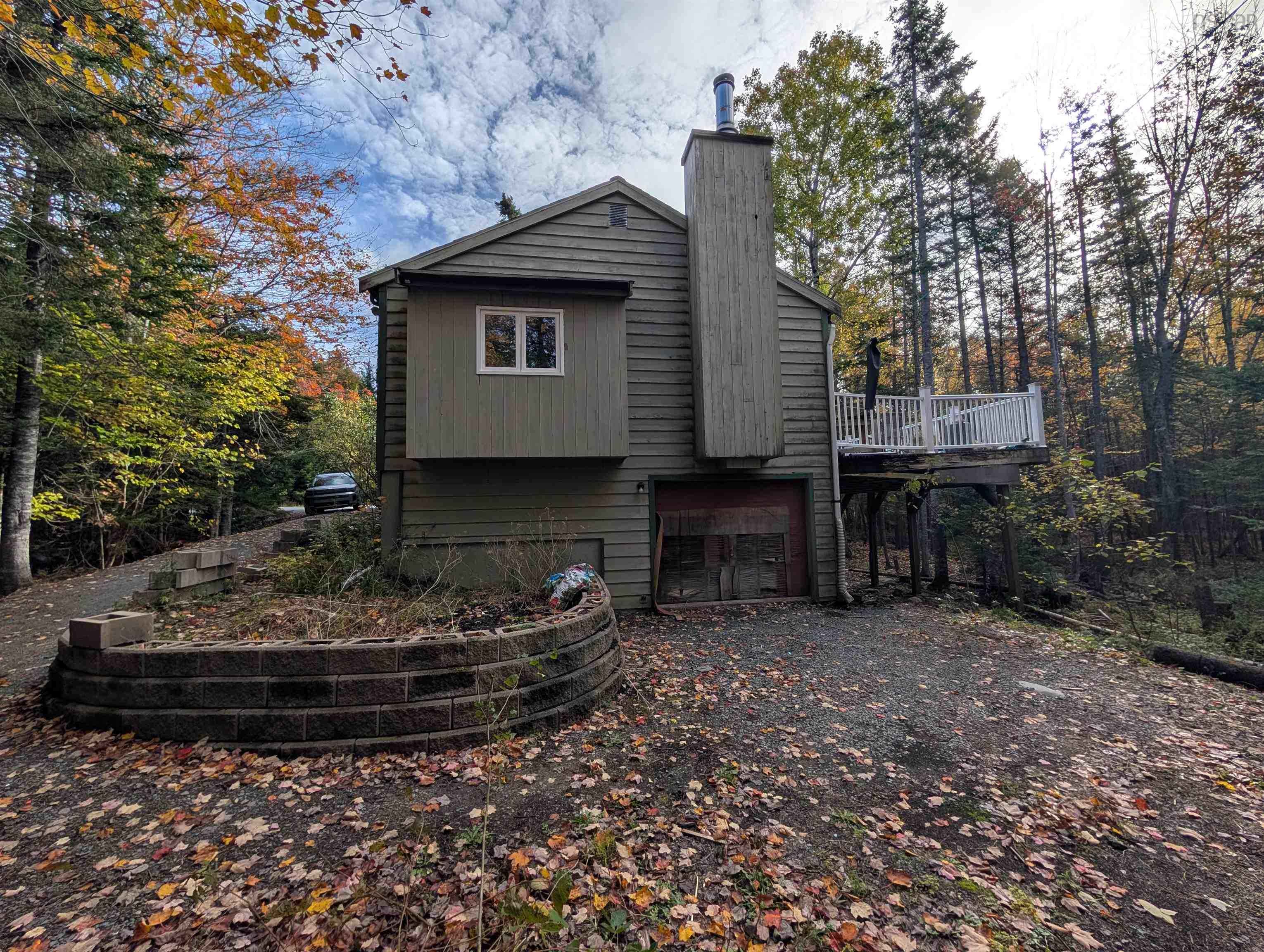 19 Foster Avenue, Fall River, NS (MLS® 202625937) — Wood-sided exterior featuring an elevated deck with white railing, a masonry chimney, a gravel driveway, and a curved retaining wall