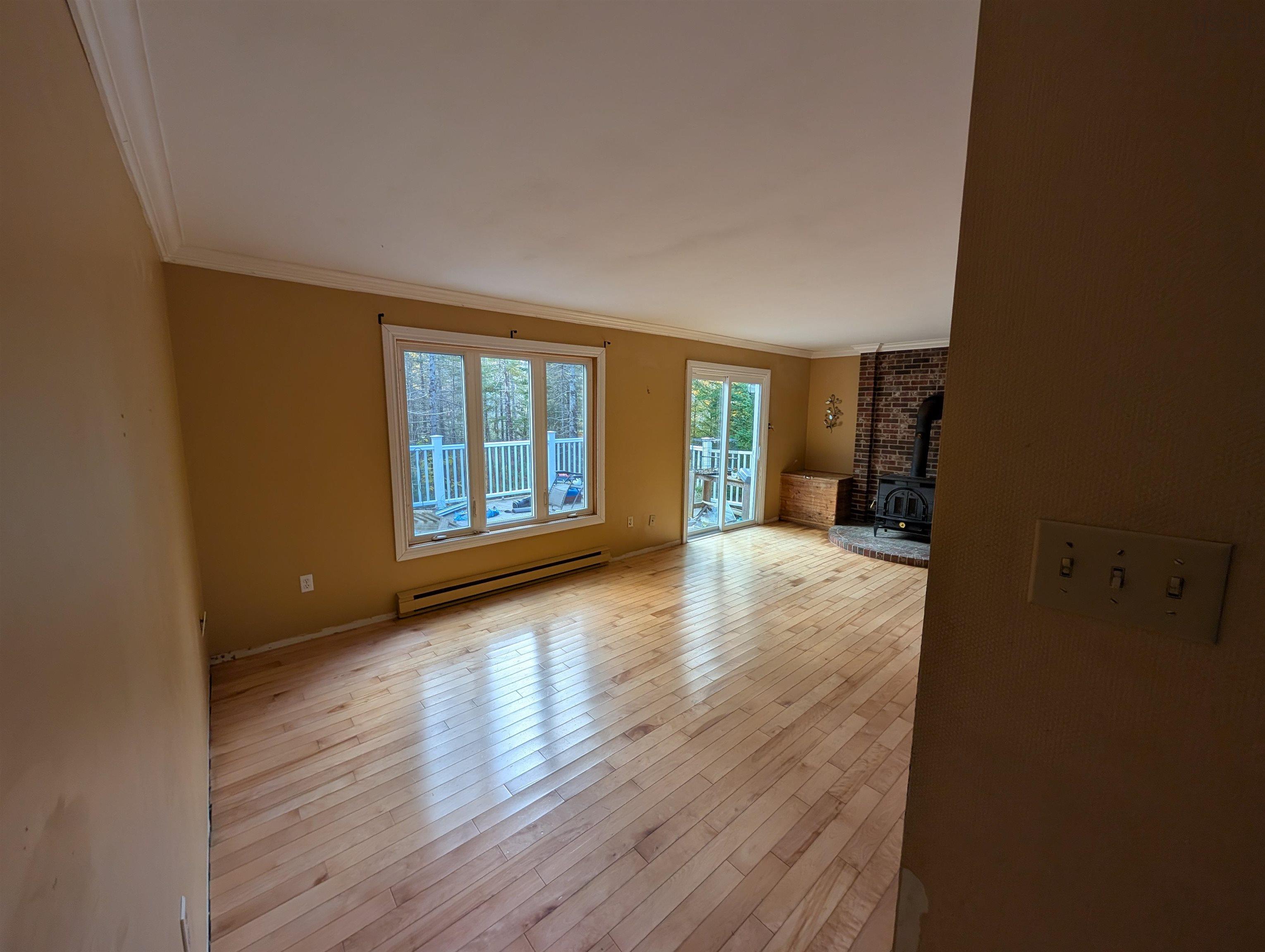 19 Foster Avenue, Fall River, NS (MLS® 202625937) — Living area featuring wood-finish flooring, a brick fireplace with a wood-burning stove, crown molding, a large picture window, and glass sliding doors
