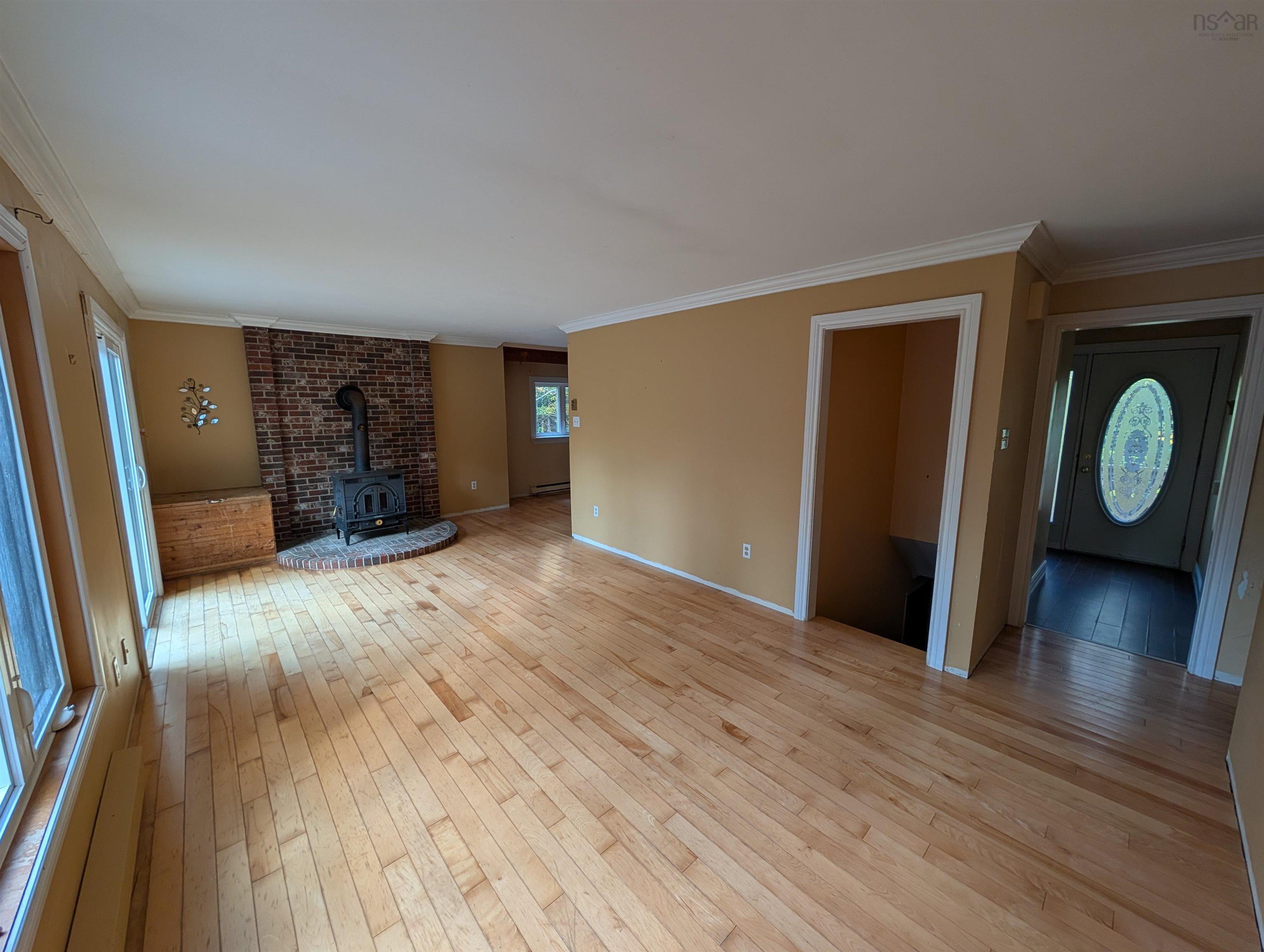 19 Foster Avenue, Fall River, NS (MLS® 202625937) — Living area featuring wood-finish flooring, a brick fireplace with a wood-burning stove, crown molding, and an exterior door with an oval glass insert