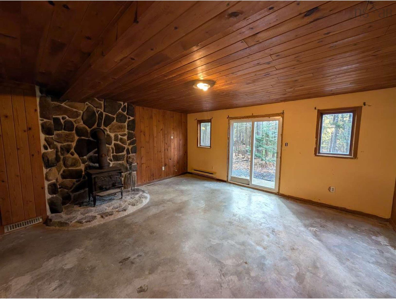 19 Foster Avenue, Fall River, NS (MLS® 202625937) — Wood-paneled ceiling, stone fireplace hearth, wood-burning stove, concrete flooring, and sliding glass door