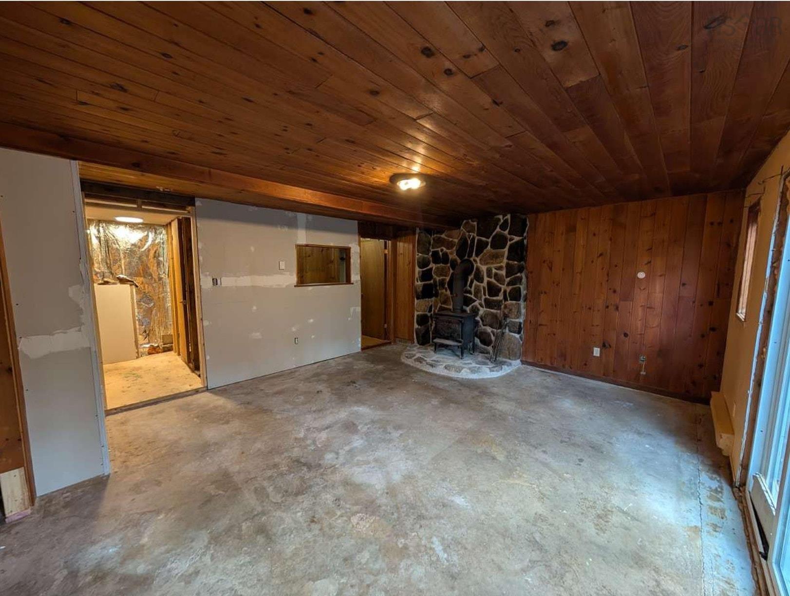 19 Foster Avenue, Fall River, NS (MLS® 202625937) — Interior room featuring wood-paneled ceiling and walls, stone fireplace surround, wood-burning stove, and flush-mount lighting