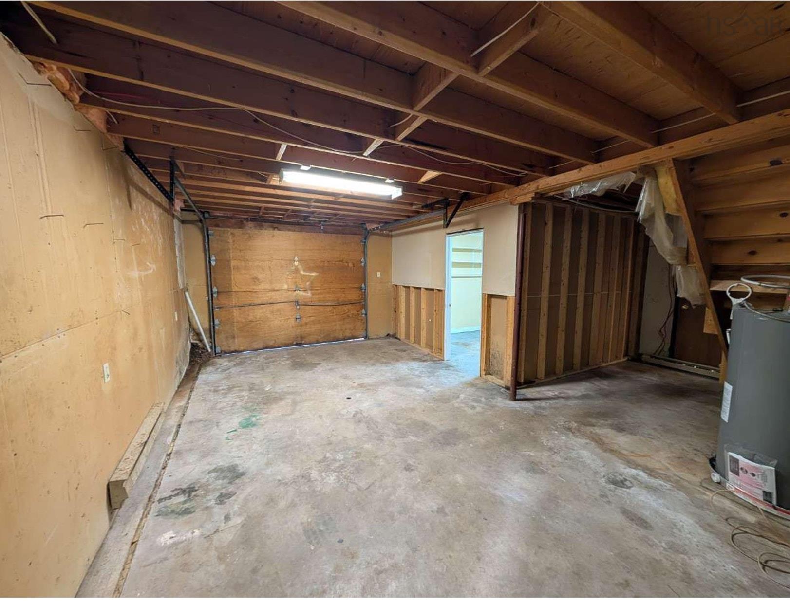 19 Foster Avenue, Fall River, NS (MLS® 202625937) — Unfinished interior space featuring exposed wood ceiling joists, concrete flooring, wooden wall paneling, and an overhead linear light fixture