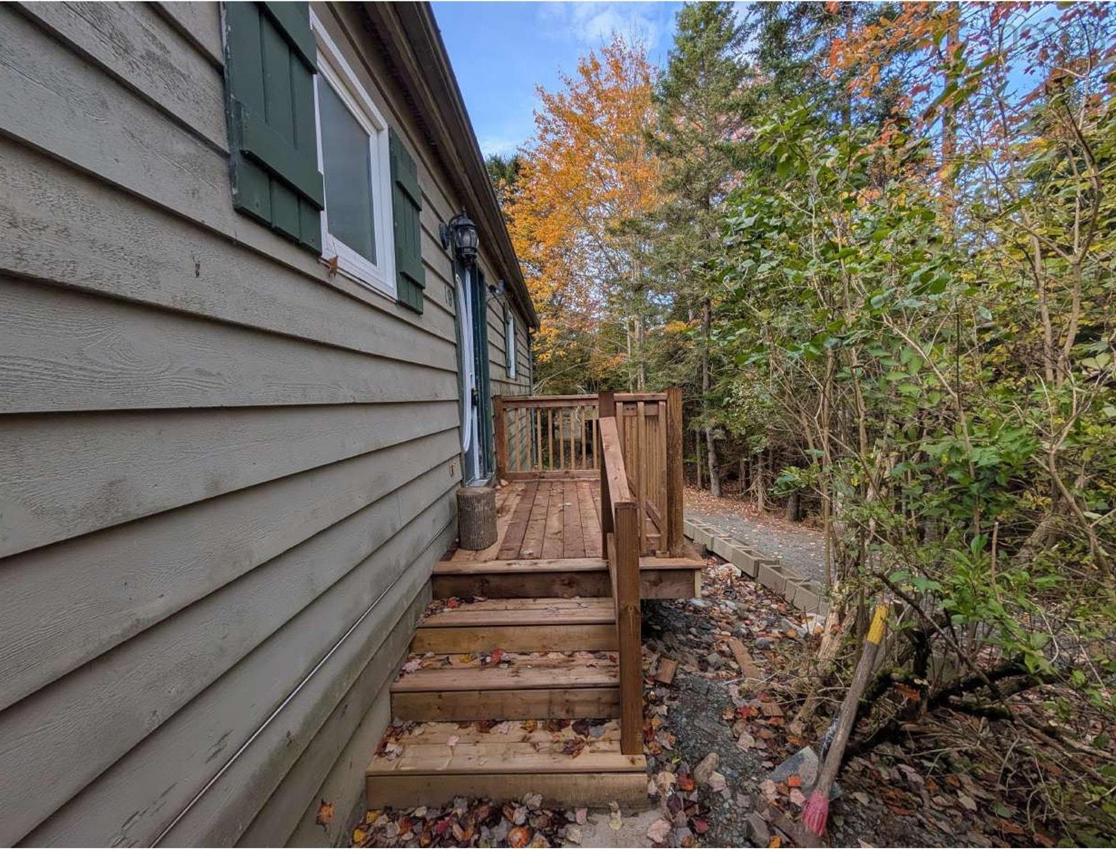 19 Foster Avenue, Fall River, NS (MLS® 202625937) — Exterior featuring horizontal siding, dark green shutters, a wood-framed deck with stairs, and a tree-lined lot