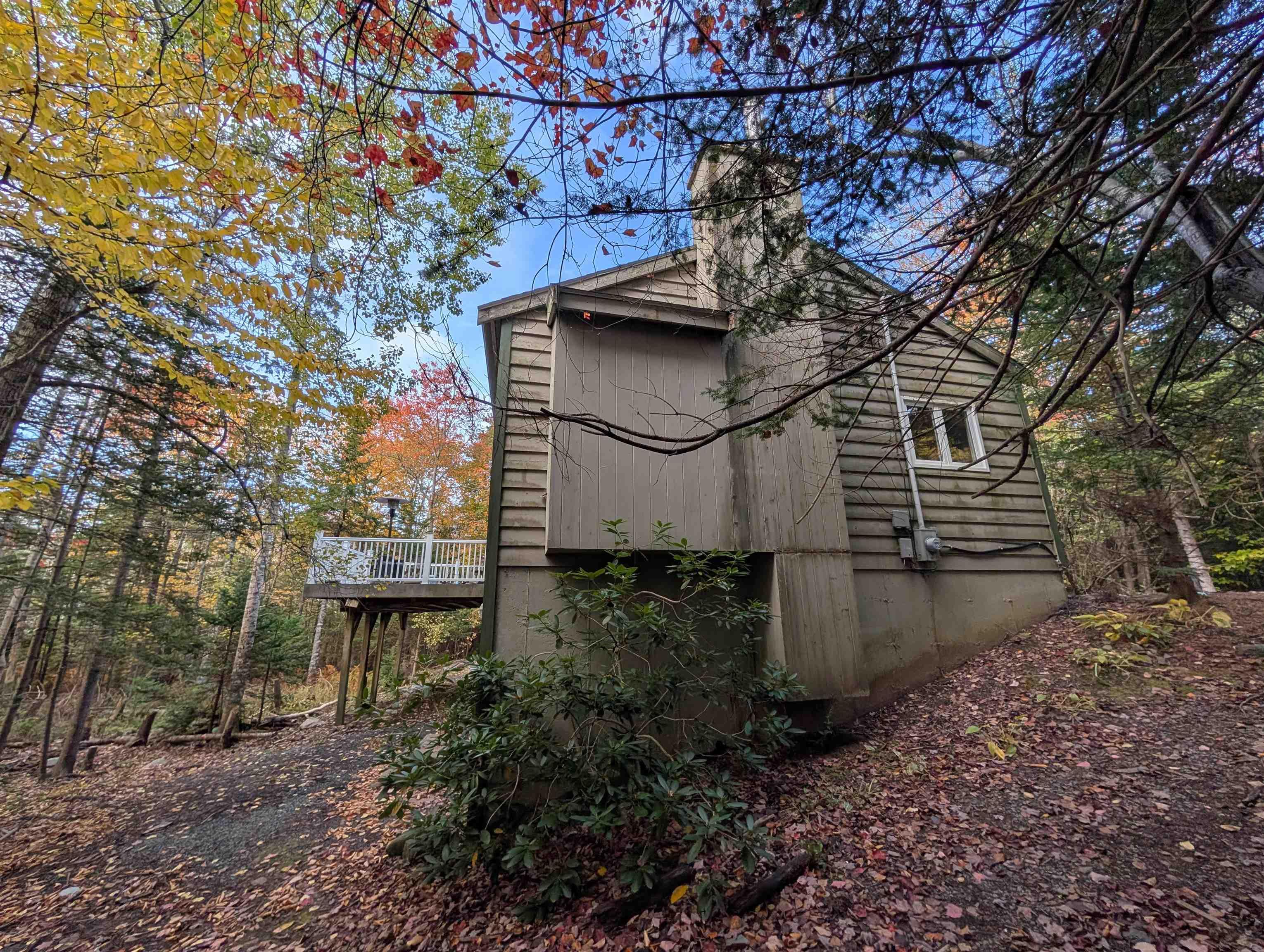 19 Foster Avenue, Fall River, NS (MLS® 202625937) — Exterior featuring horizontal lap siding, a chimney, and a raised wooden deck with white railings, set against a wooded landscape
