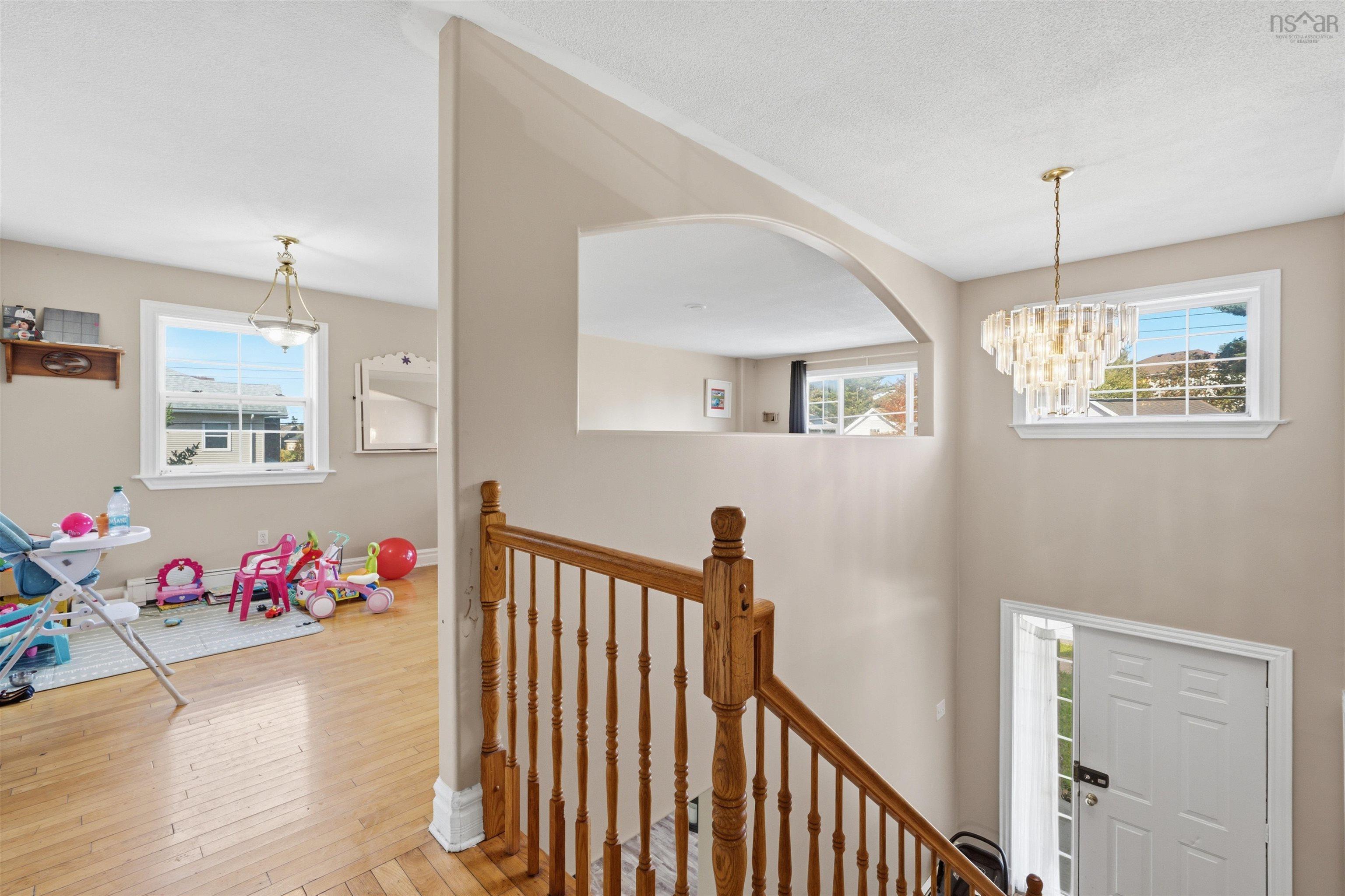 34 Lancaster Drive, Clayton Park, NS (MLS® 202626151) — Interior staircase with wood balustrades and a carved wood handrail, featuring wood-finish flooring, two decorative glass pendant light fixtures, and a wall cutout with an arched architectural detail