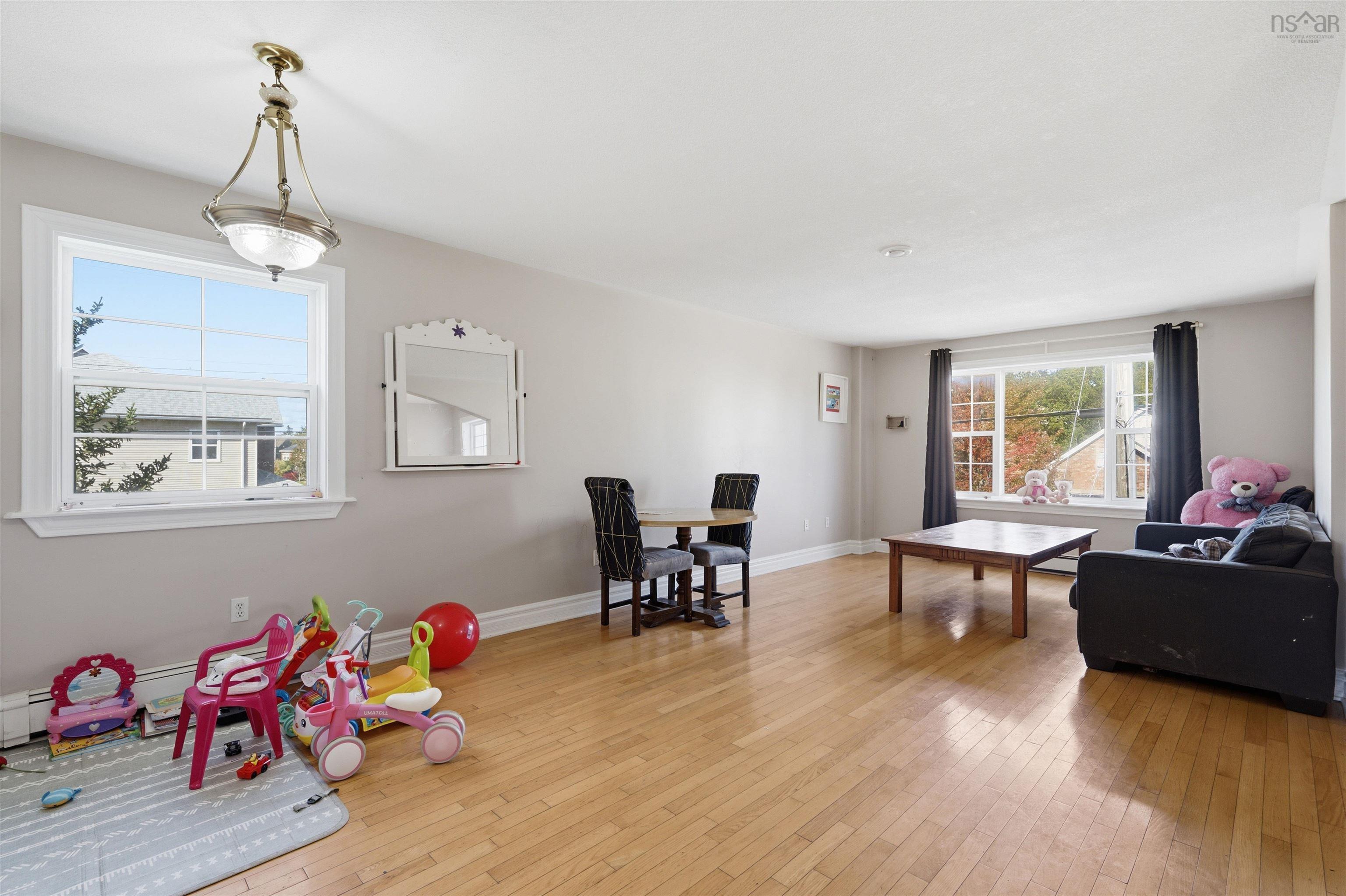 34 Lancaster Drive, Clayton Park, NS (MLS® 202626151) — Living area featuring wood-finish flooring, two multi-pane windows, and a central tiered pendant light fixture