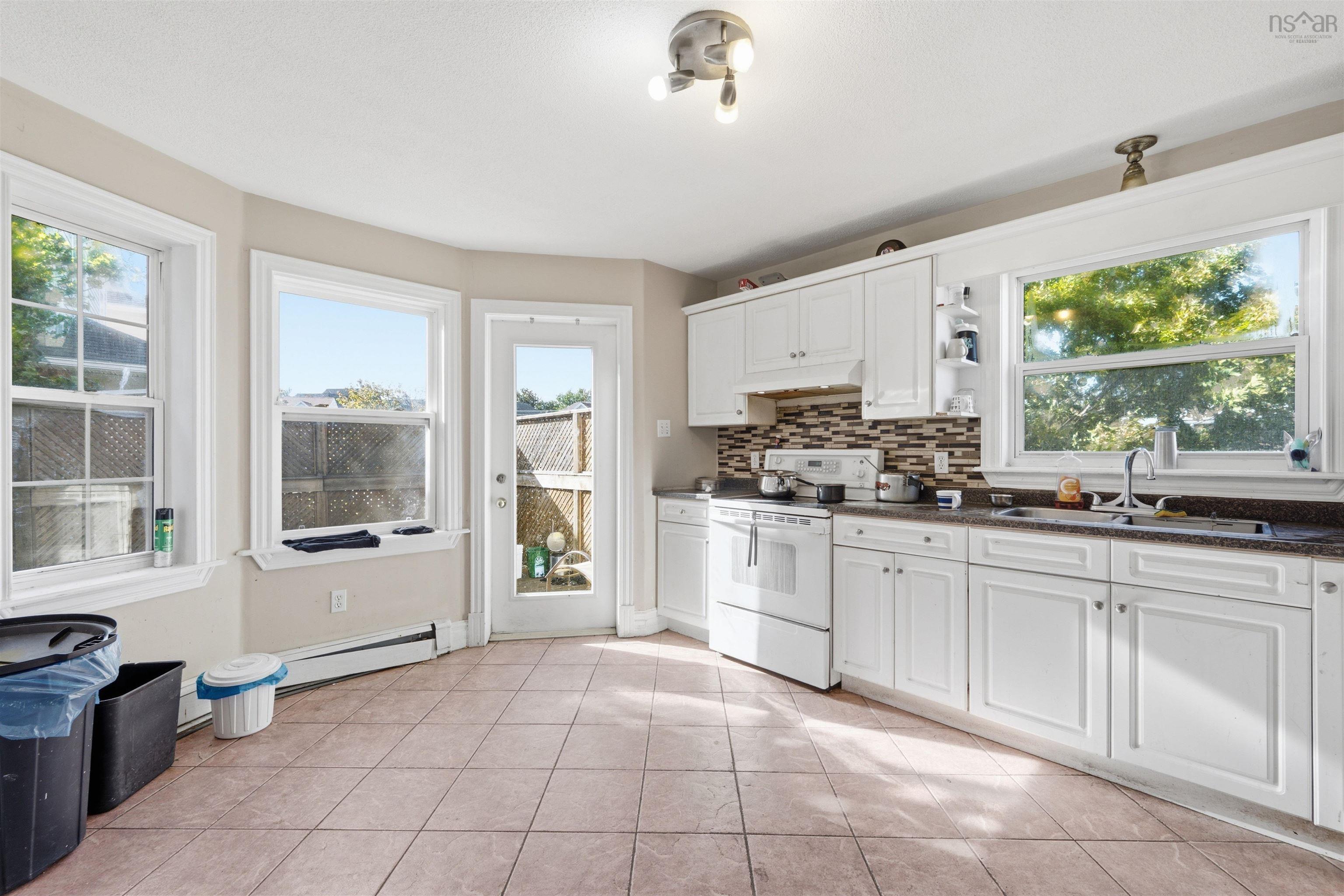34 Lancaster Drive, Clayton Park, NS (MLS® 202626151) — Kitchen featuring white cabinetry, mosaic tile backsplash, dark solid-surface countertops, tile flooring, and a glass-paneled exterior door