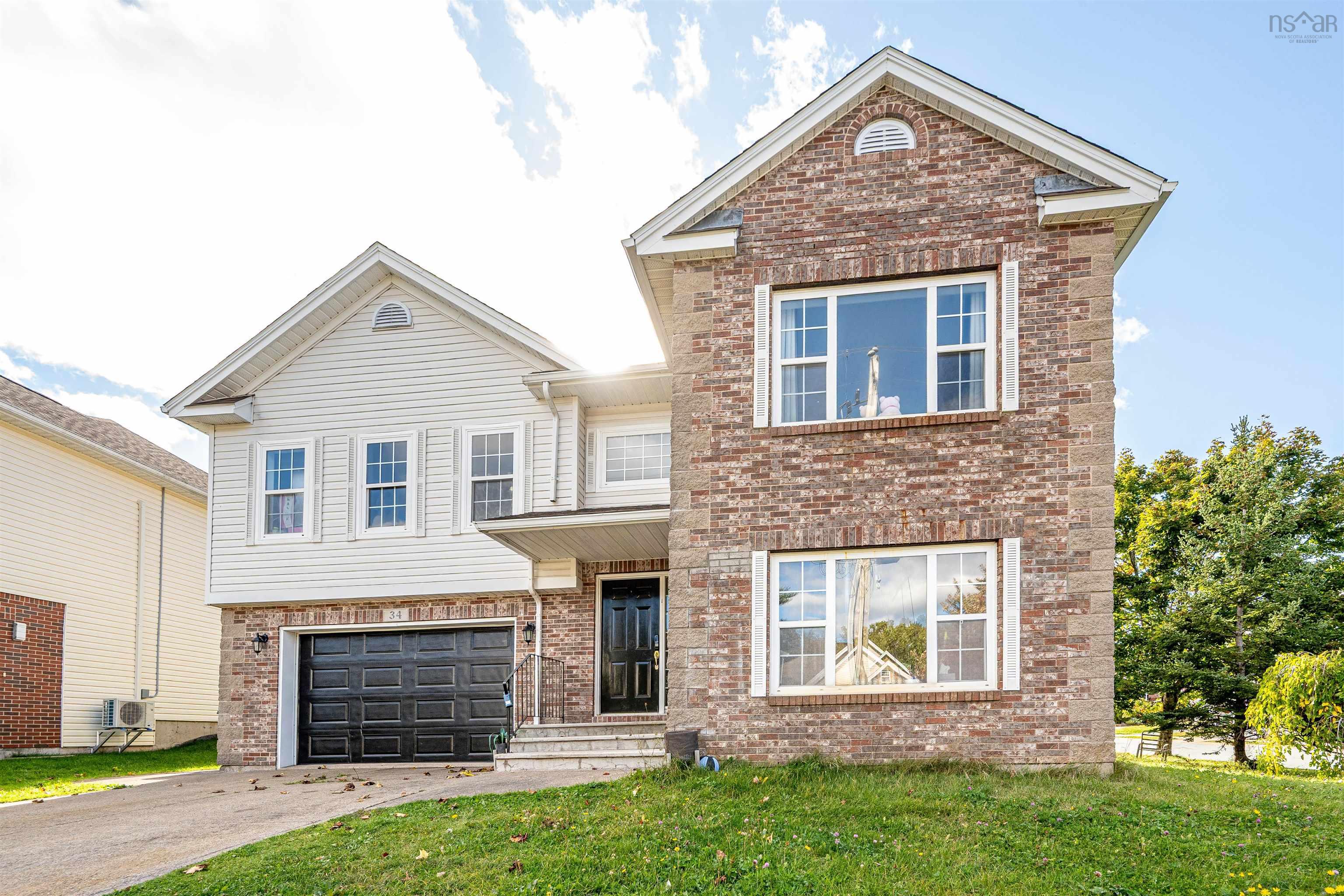 34 Lancaster Drive, Clayton Park, NS (MLS® 202626151) — Two-story exterior featuring a brick and horizontal siding facade, multi-gabled roofline, double-car garage with black door, and large rectangular windows with shutters