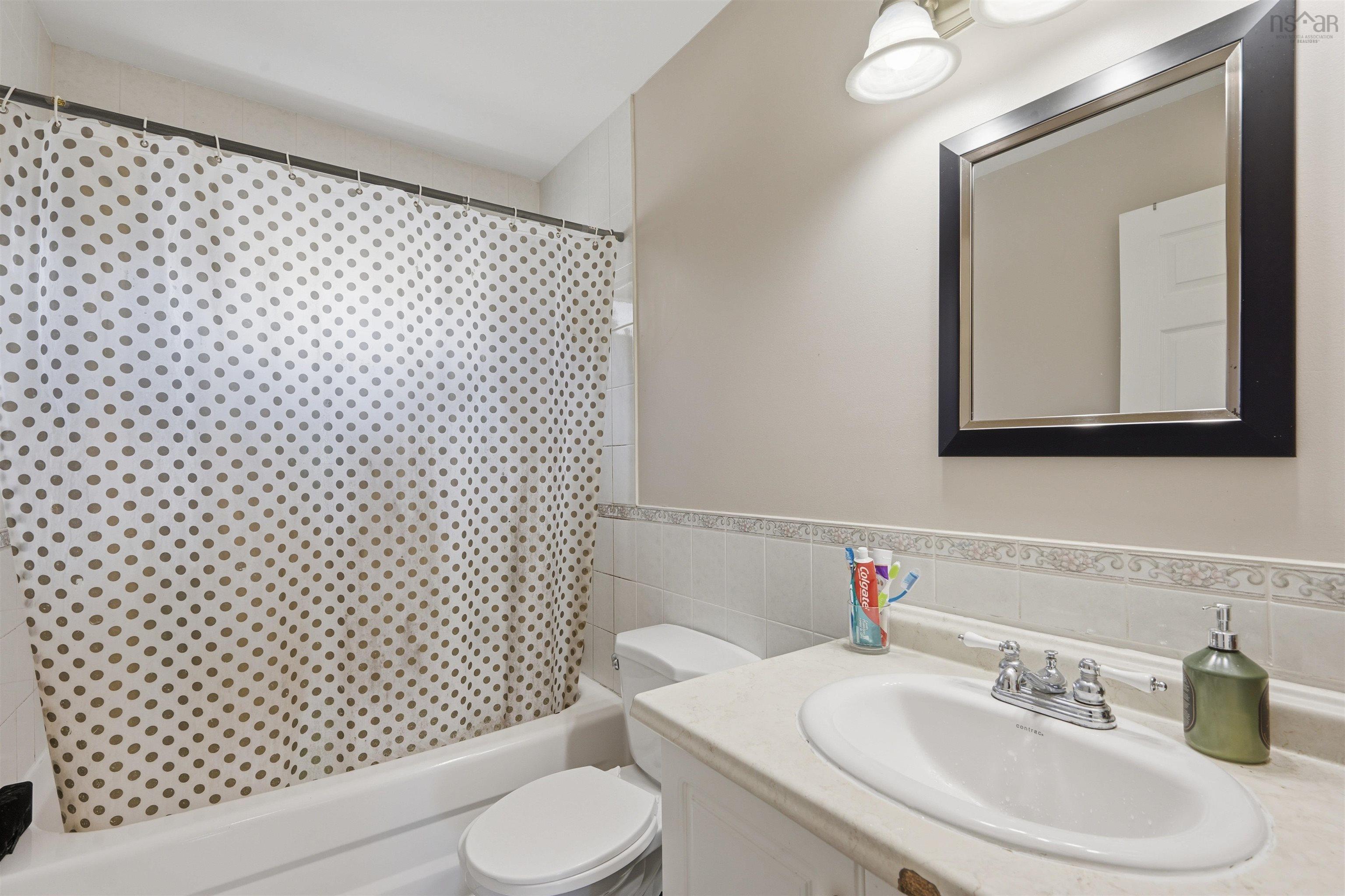 34 Lancaster Drive, Clayton Park, NS (MLS® 202626151) — Bathroom featuring a solid-surface vanity countertop, drop-in sink with chrome dual-handle faucet, wall-mounted mirror with a black frame, and a tiled shower surround