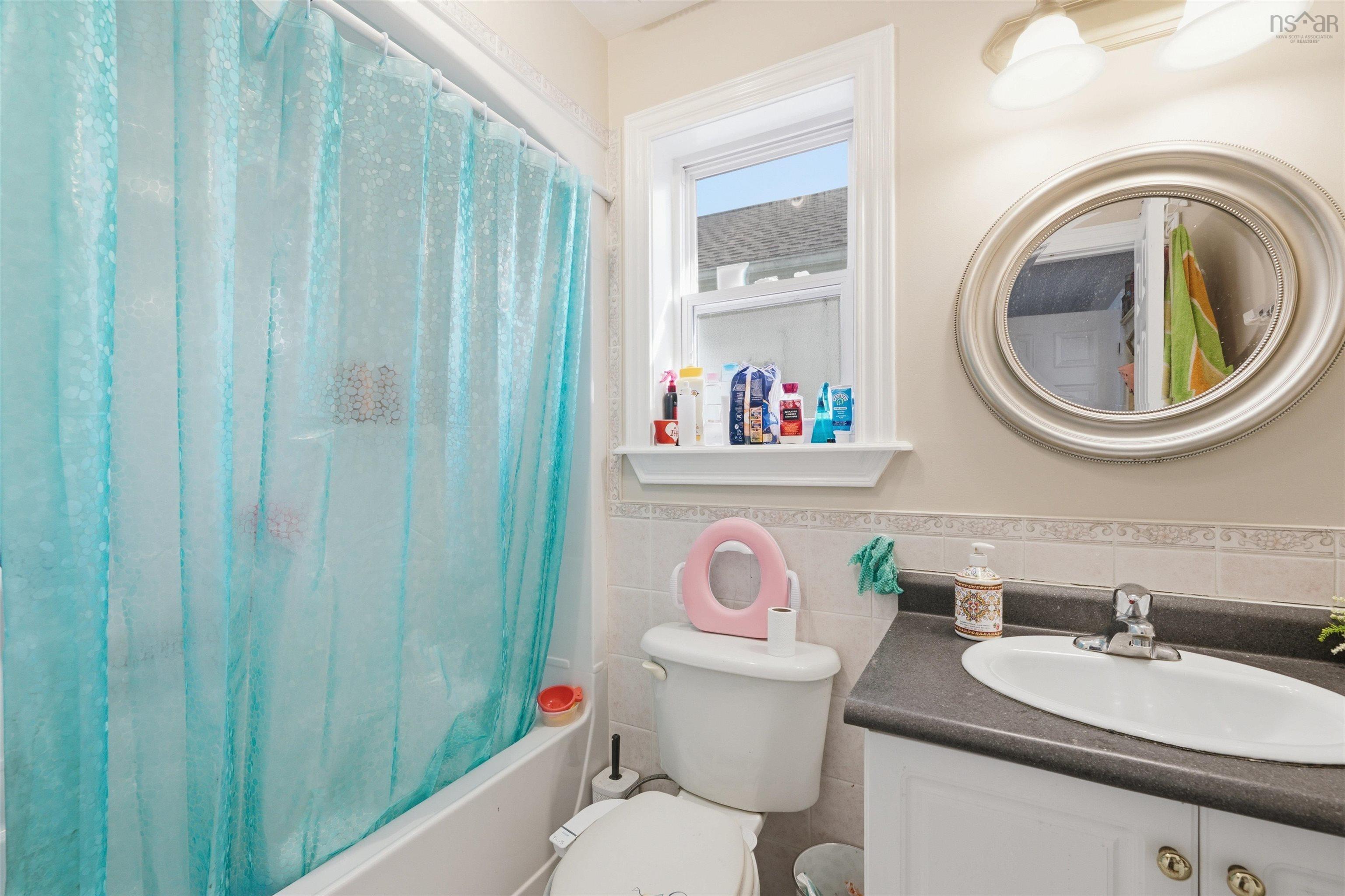 34 Lancaster Drive, Clayton Park, NS (MLS® 202626151) — Bathroom featuring an oval-mounted vanity mirror, white cabinetry with dark countertop, integrated oval sink, and decorative wall tile trim
