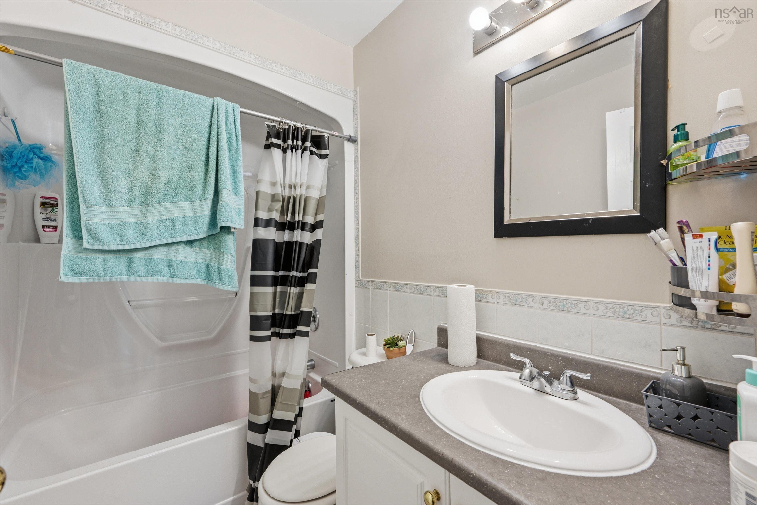 34 Lancaster Drive, Clayton Park, NS (MLS® 202626151) — Bathroom featuring a white bathtub and shower surround, vanity with a solid-surface countertop and integrated oval basin, chrome-finish faucet, and a wall-mounted framed mirror