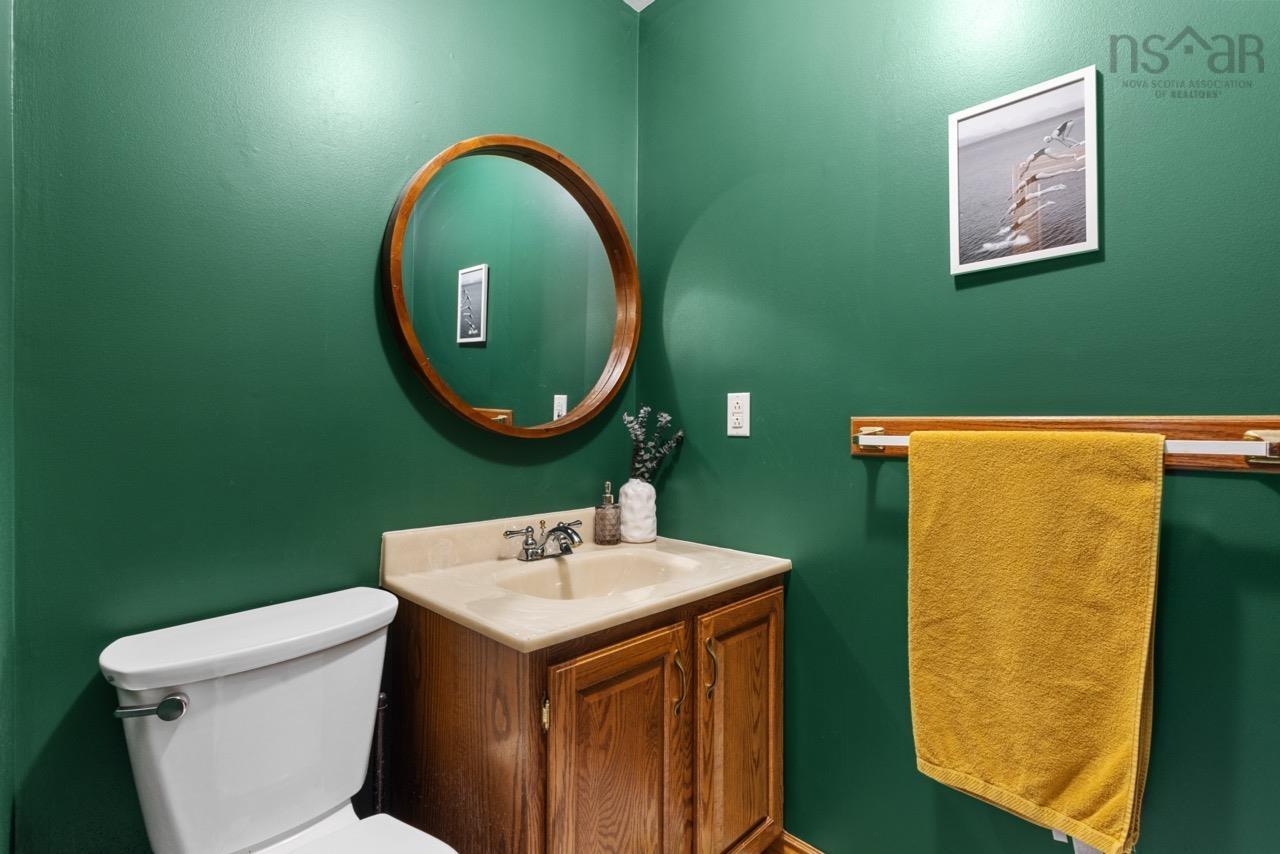 24 Rossi Drive, Dartmouth, NS (MLS® 202626410) — Powder room featuring a wood vanity with a stone-composite countertop, integrated sink, chrome dual-handle faucet, and a circular wooden-frame mirror