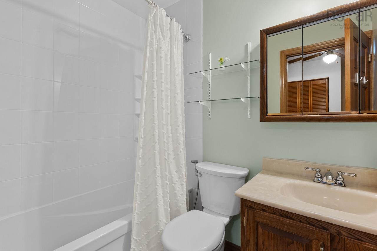 24 Rossi Drive, Dartmouth, NS (MLS® 202626410) — Bathroom featuring a tub-shower combination with white tile surround, wooden vanity with an integrated sink, metal hardware, a medicine cabinet with a wood frame, and wall-mounted glass shelving