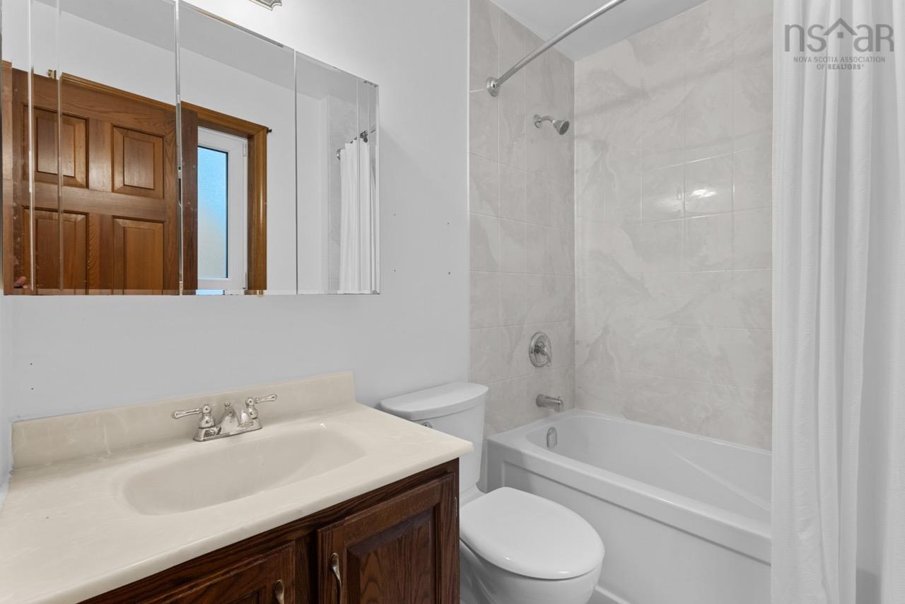 24 Rossi Drive, Dartmouth, NS (MLS® 202626410) — Bathroom featuring a wood-finish vanity with a stone-composite countertop, integrated sink, mirrored medicine cabinet, and a bathtub with tile-surround walls