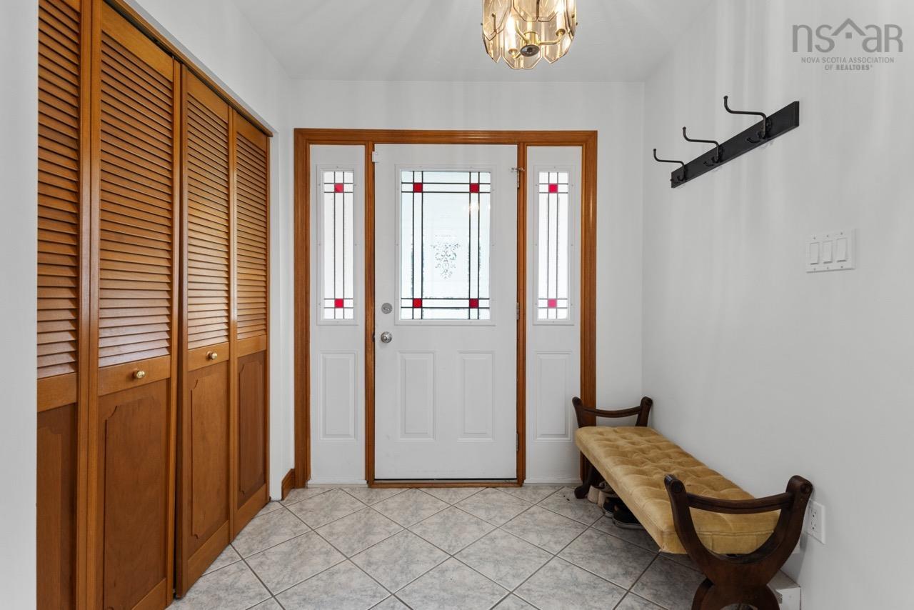 24 Rossi Drive, Dartmouth, NS (MLS® 202626410) — Entryway featuring a solid door with decorative glass paneling, sidelights with red accent detailing, wood-finish louvered closet doors, neutral tile flooring, and a flush-mount light fixture