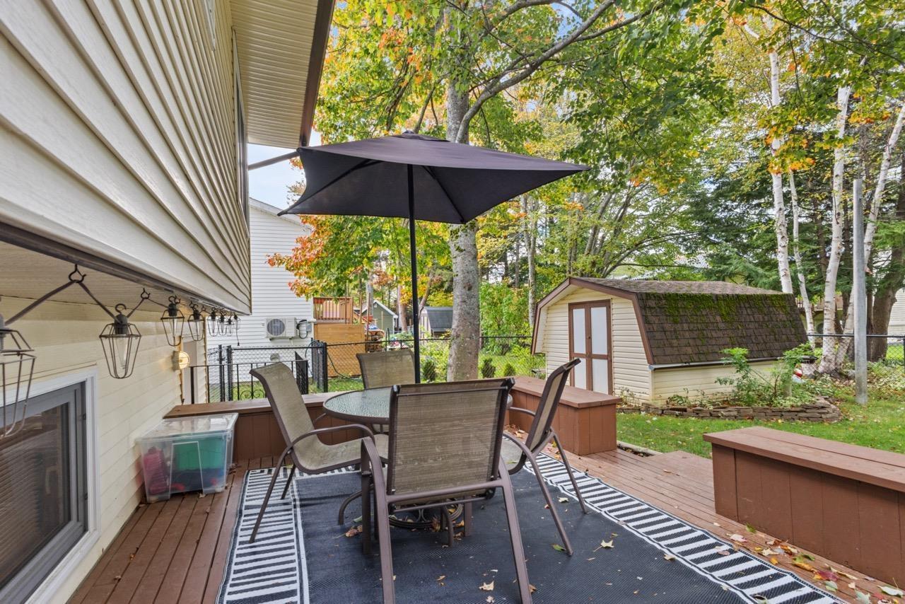 24 Rossi Drive, Dartmouth, NS (MLS® 202626410) — Raised wood deck featuring integrated built-in benches, exterior wall-mounted lighting, and a detached storage shed set against a backdrop of mature trees