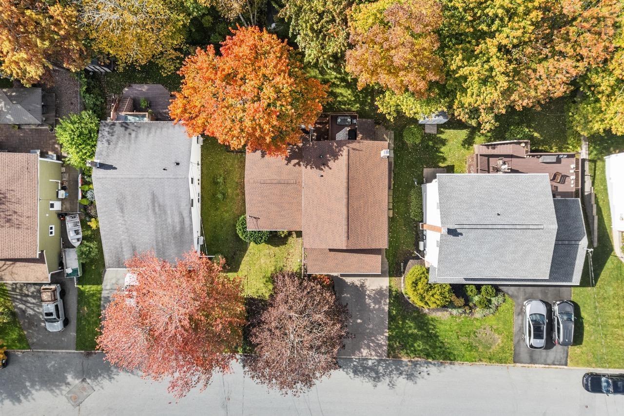24 Rossi Drive, Dartmouth, NS (MLS® 202626410) — Aerial perspective of the property featuring a paved driveway, a shingled roof, mature trees, and a wooden rear deck