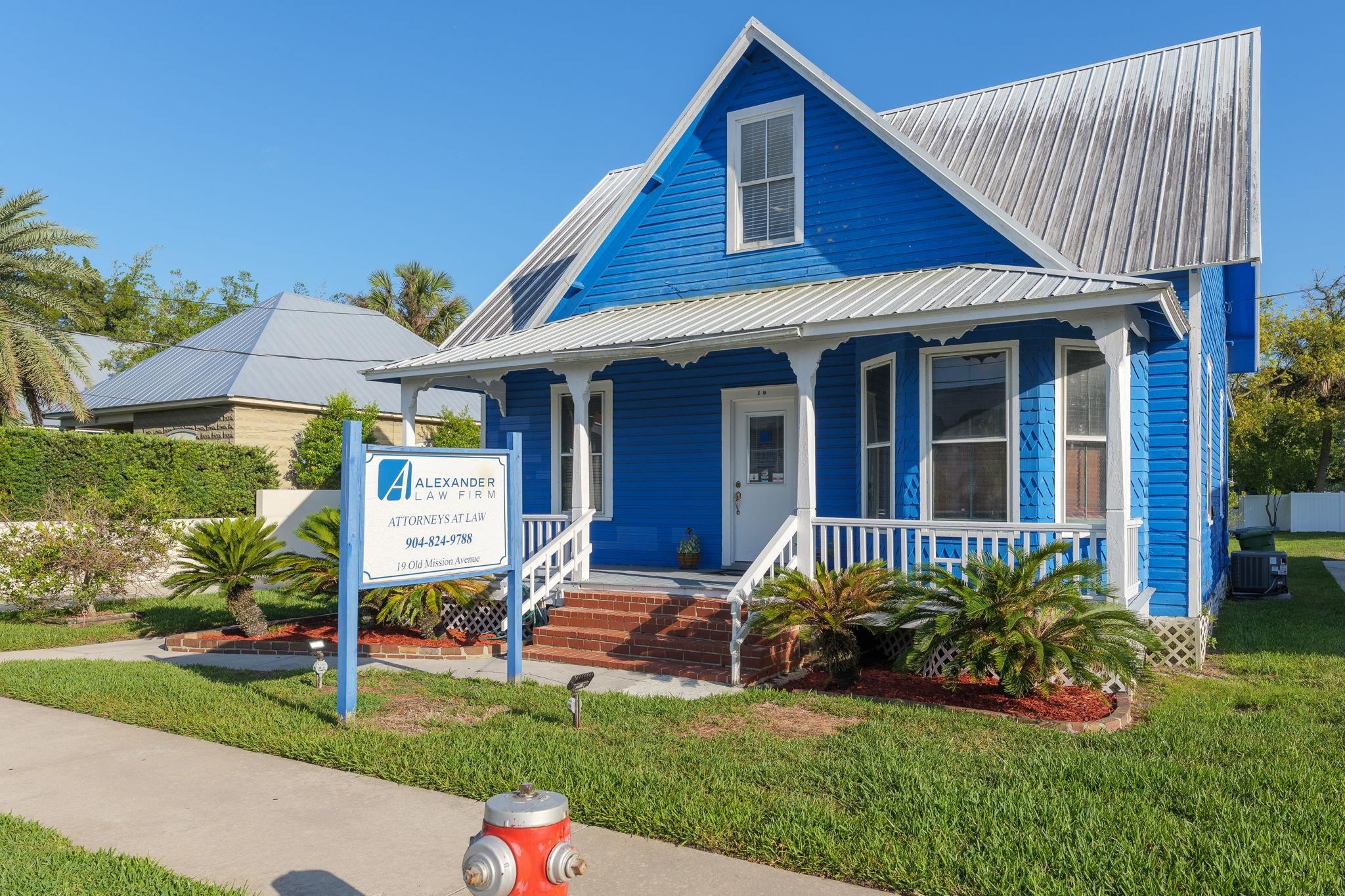 Bright blue siding exterior featuring a covered porch with white railings, a metal roof, and established landscaping Front Of Structure