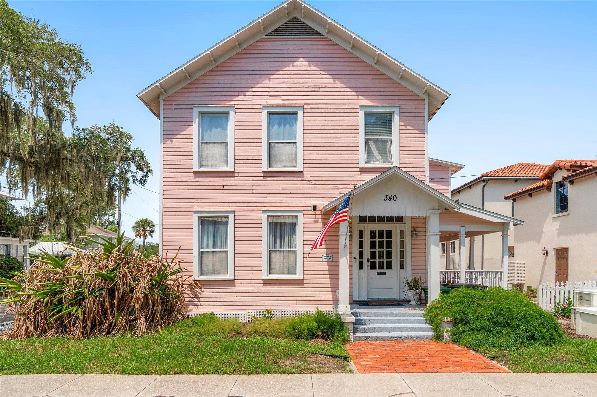 Two-story residence with pink wood siding, a white columned front porch, and a brick pathway Front Of Structure