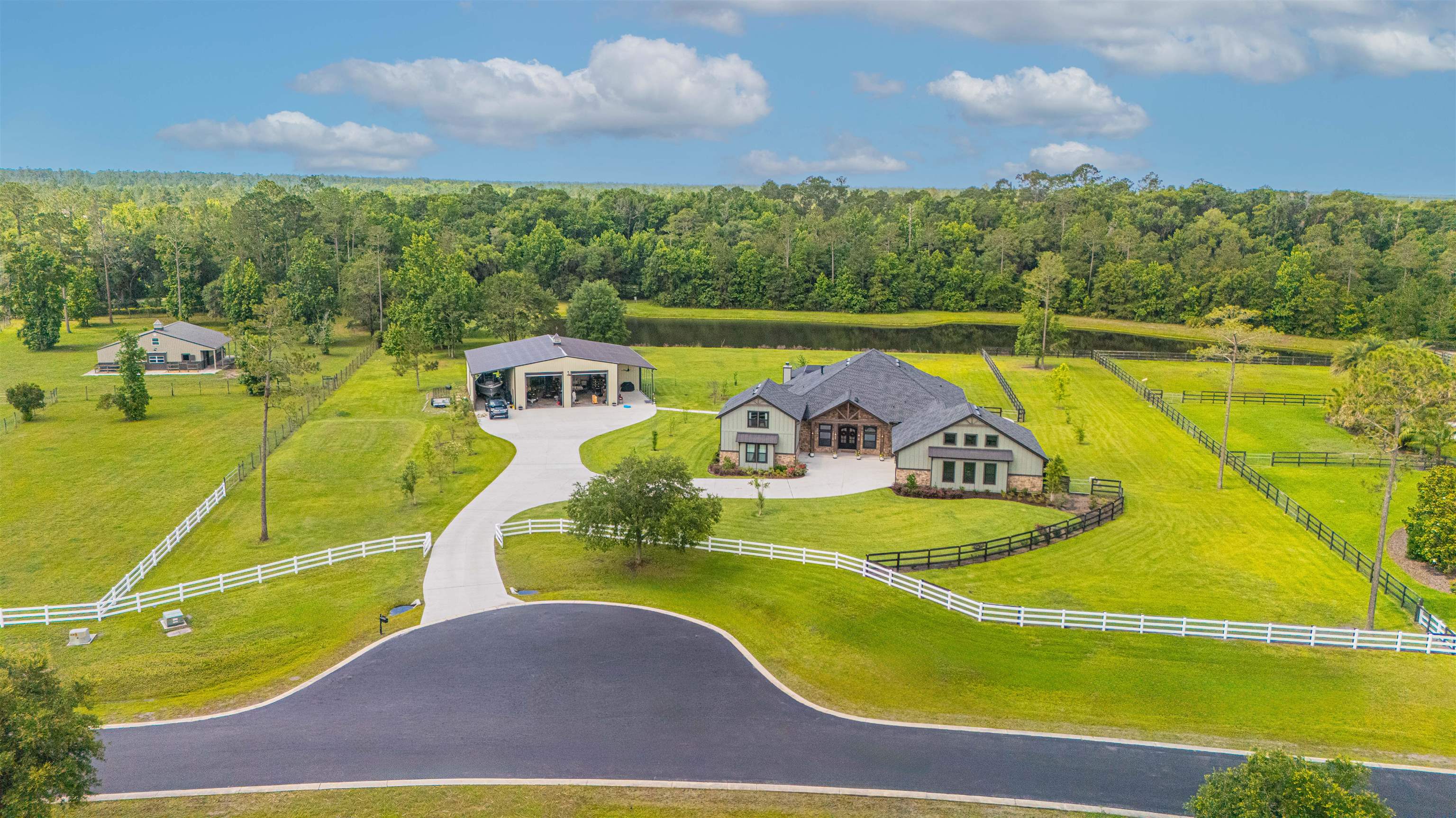 Expansive property featuring a contemporary residence, a detached garage structure, a pond, and surrounding mature trees Aerial View