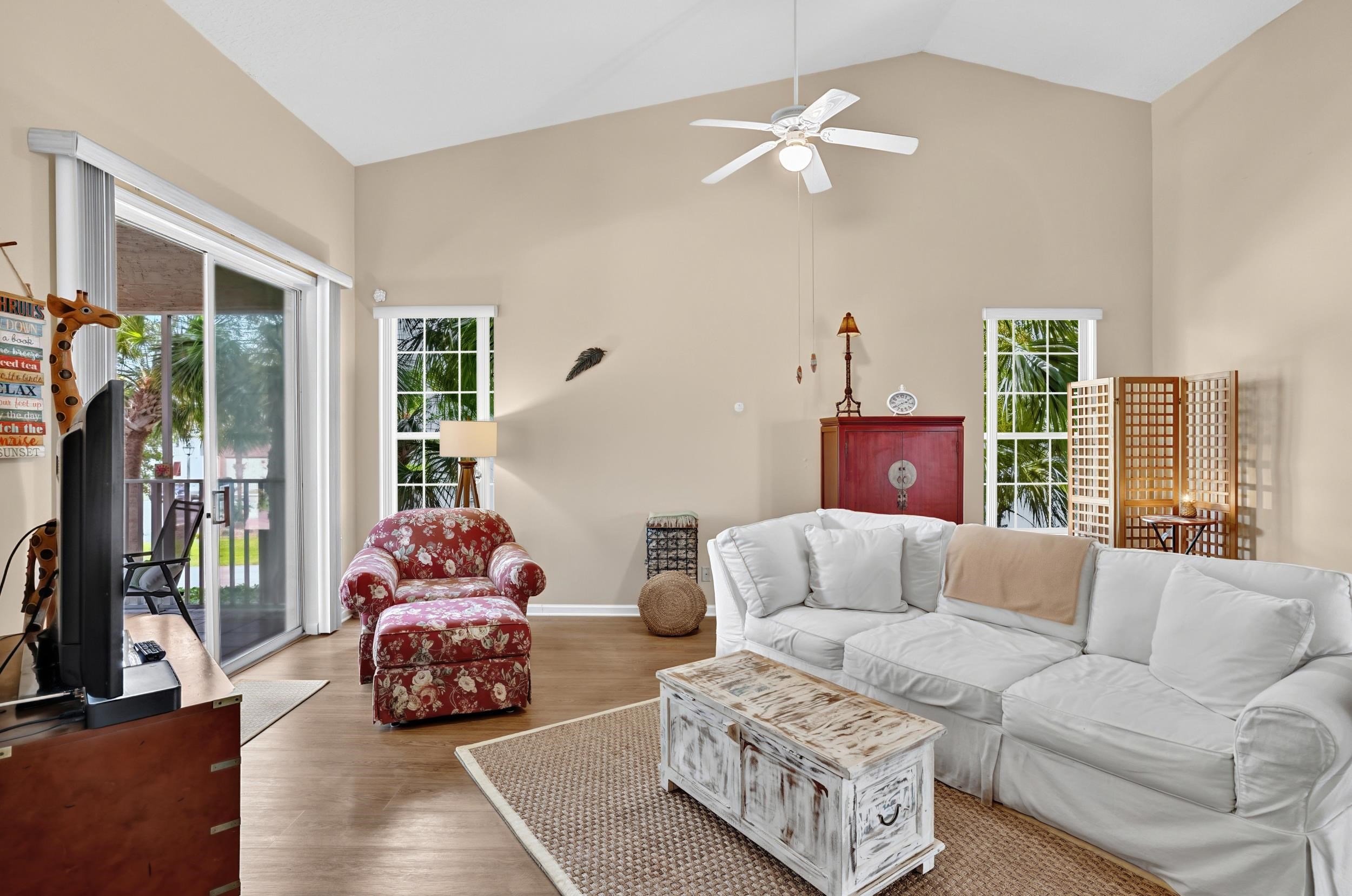 Vaulted ceilings enhance this living space featuring wood-finish flooring, a ceiling fan, and multiple windows Living Room