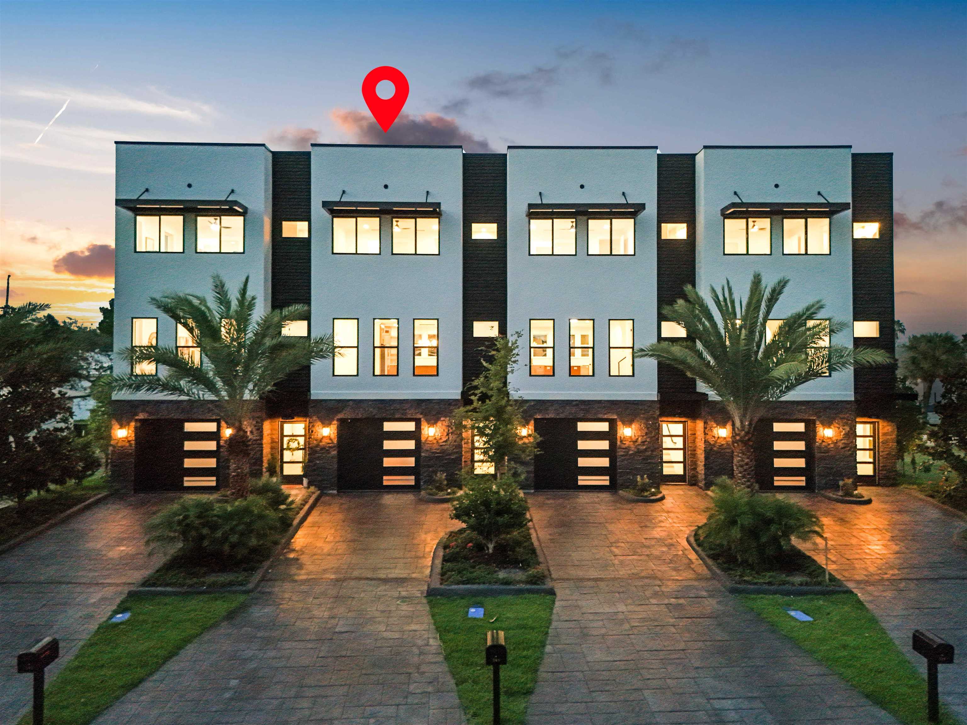 Modern townhome facade featuring a two-tone exterior, dark stone accents, contemporary garage doors with horizontal lites, and a stamped concrete driveway Front Of Structure