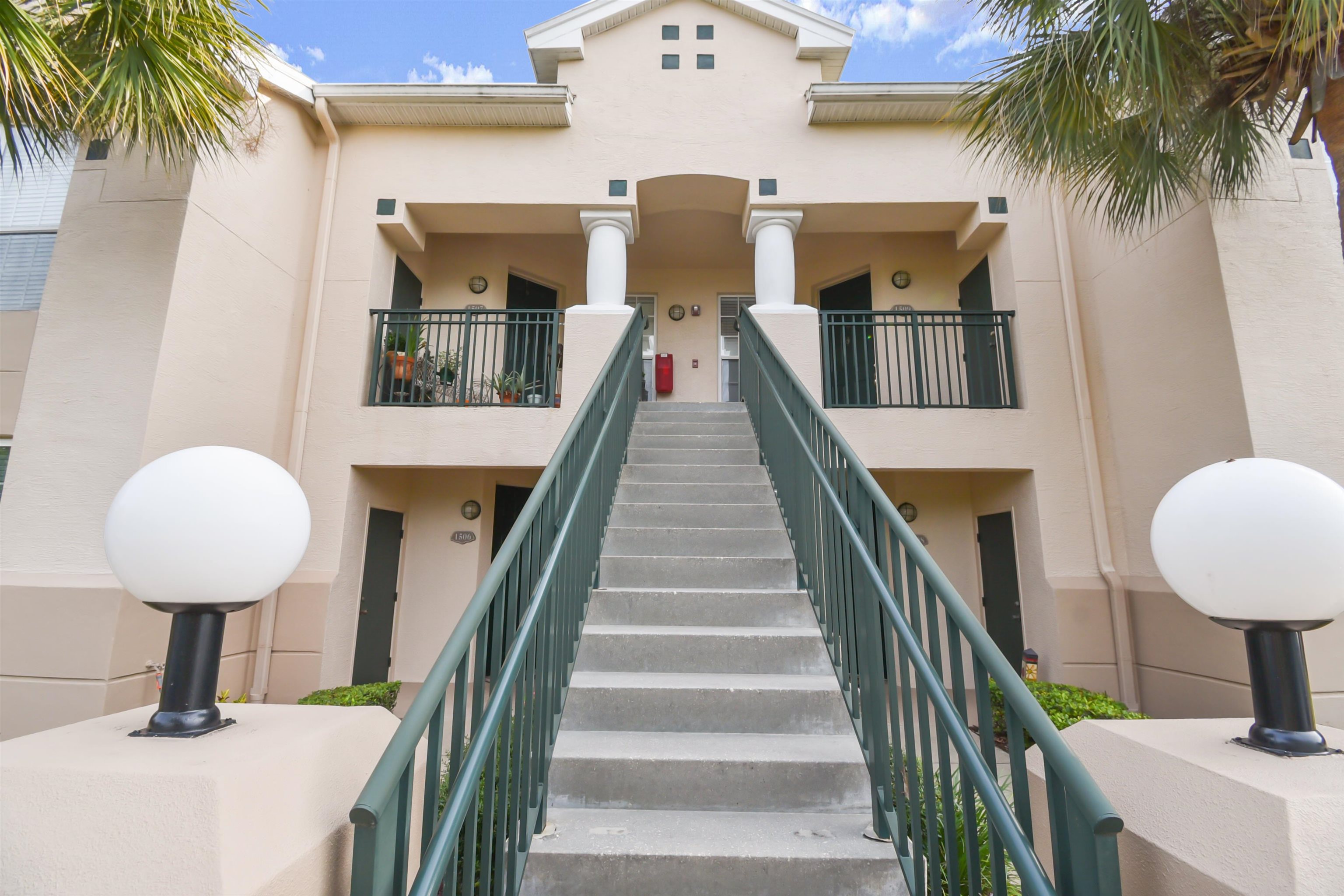 Multi-story stucco exterior featuring a prominent staircase with dark green railings Stairs