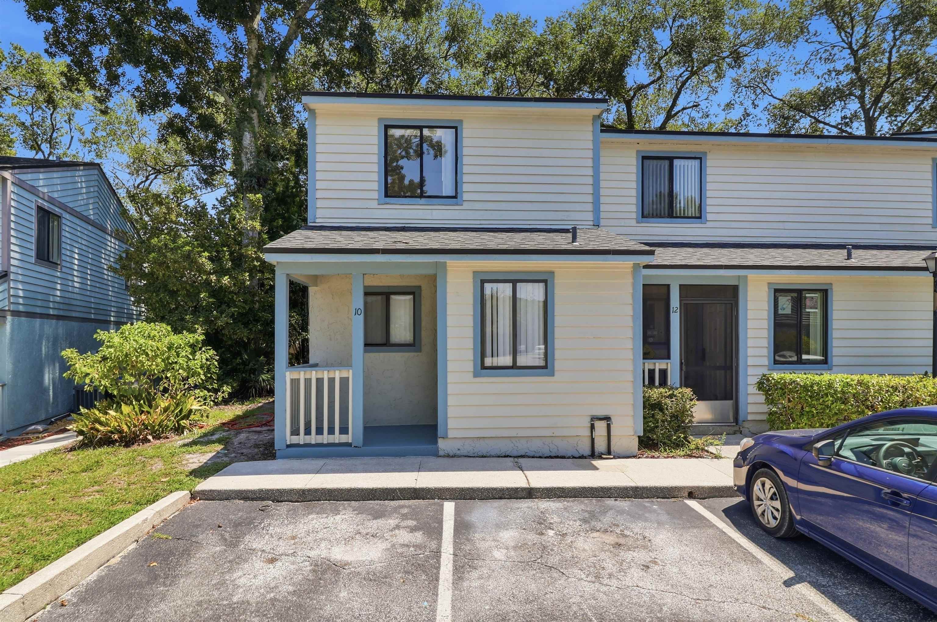 Two-story residence featuring light-colored siding, dark-trimmed windows, a covered entry, and a paved parking area Front Of Structure