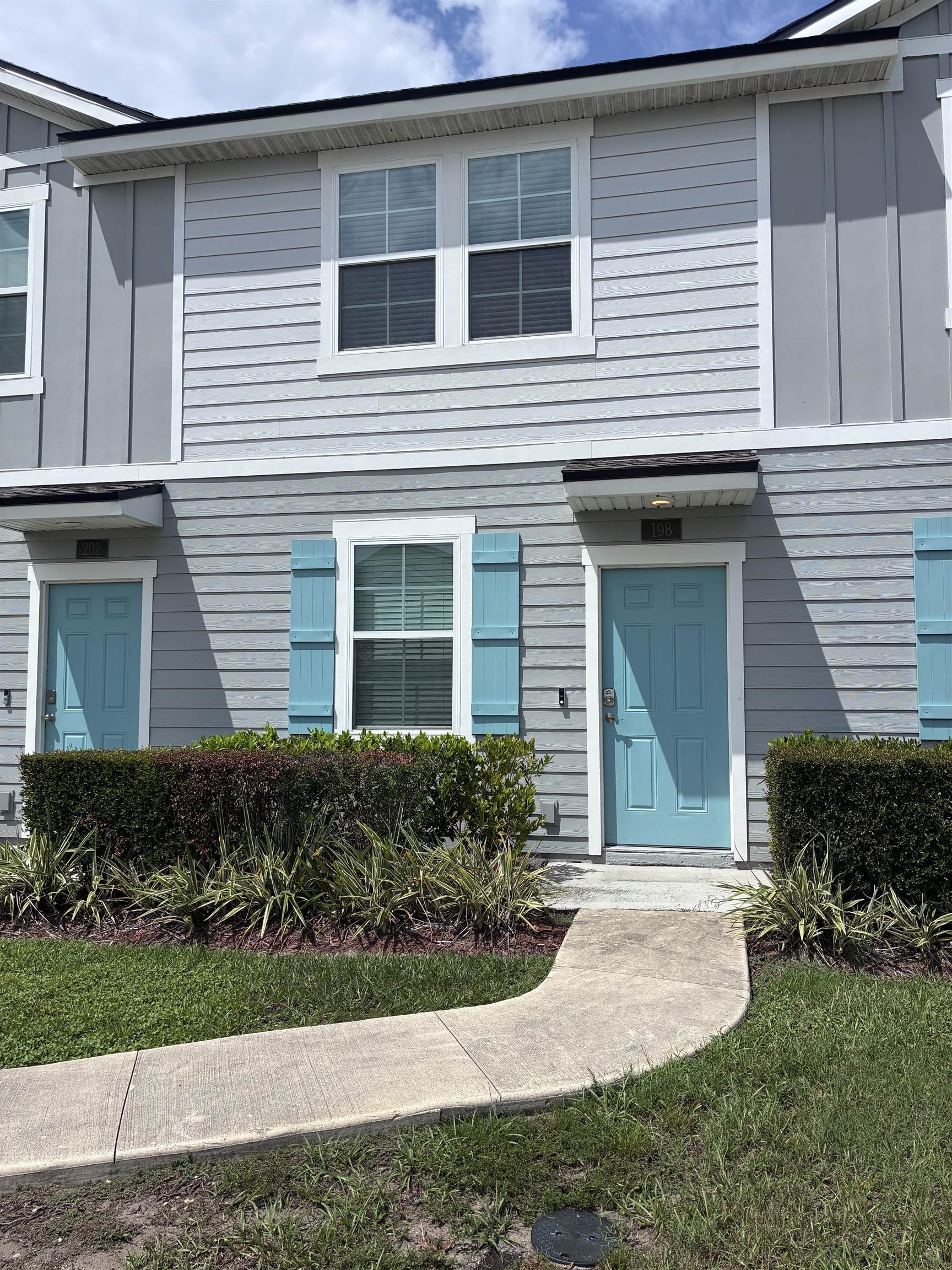 Siding exterior with contrasting trim, a curved concrete pathway, and established front landscaping Front Of Structure