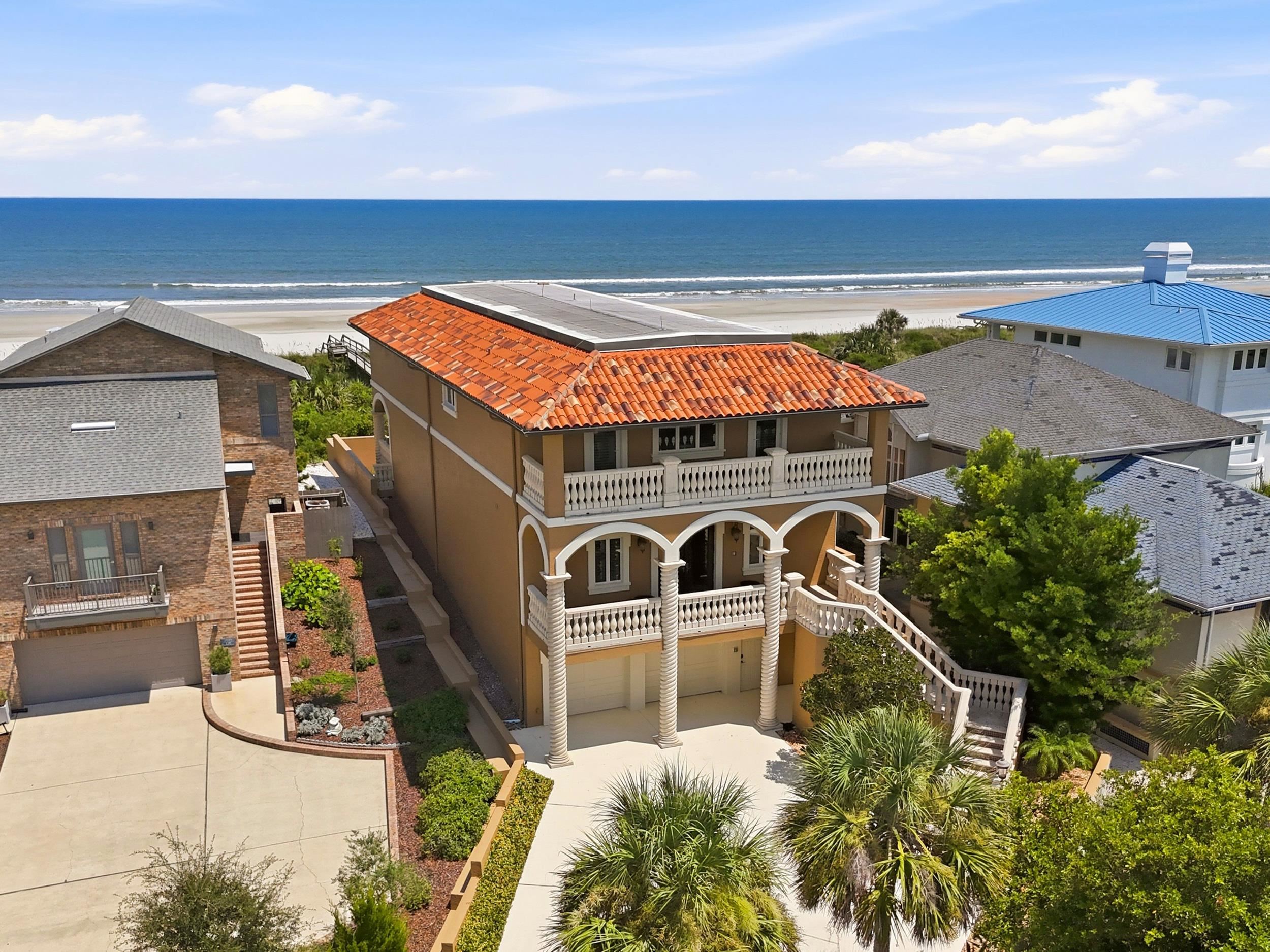Oceanfront residence featuring a terra cotta tile roof, multiple balconies, an arched portico, and a white balustrade Front Of Structure