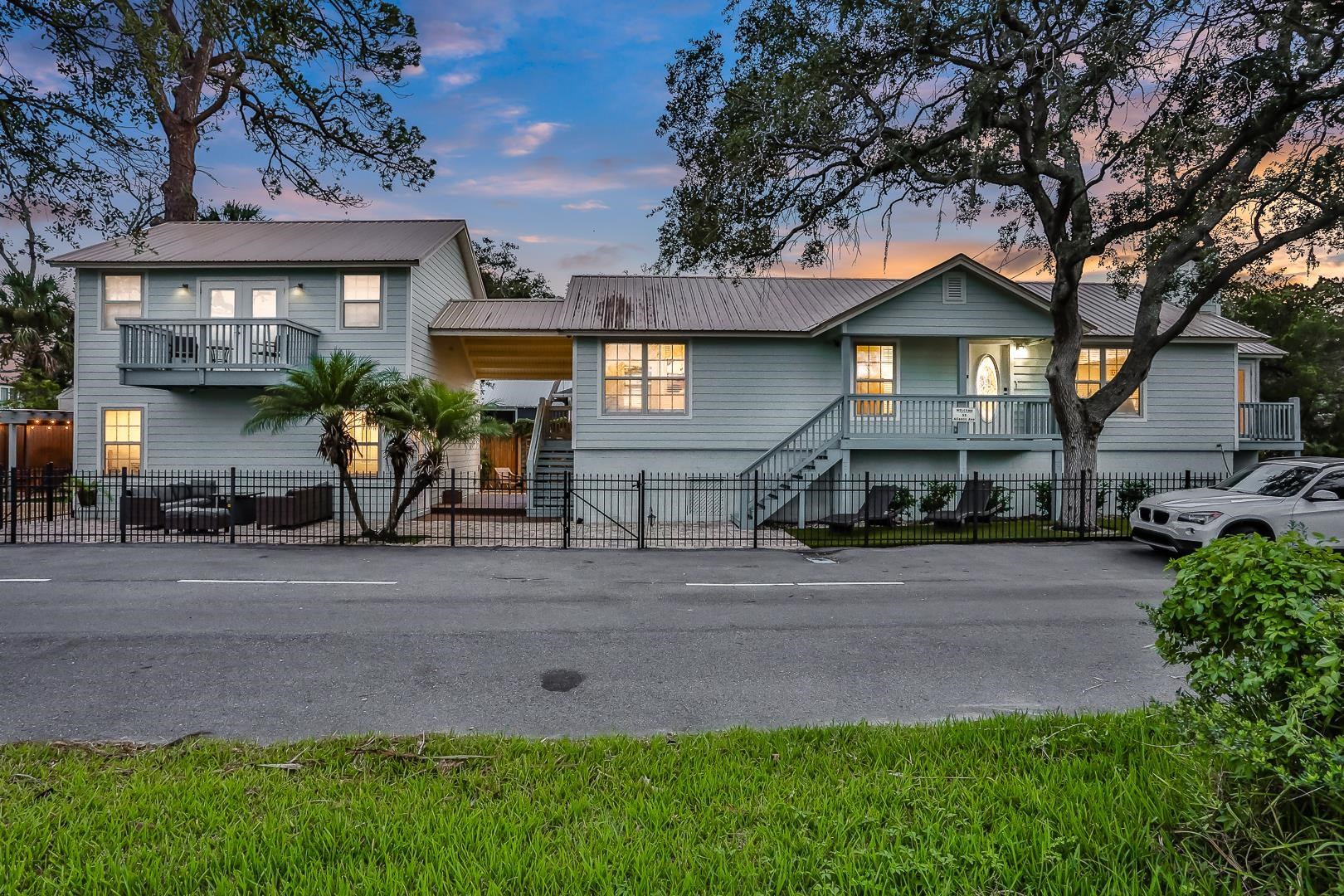 Light blue exterior siding, metal roof, wrought iron style fencing, elevated entry with steps, and a second-story balcony Front Of Structure