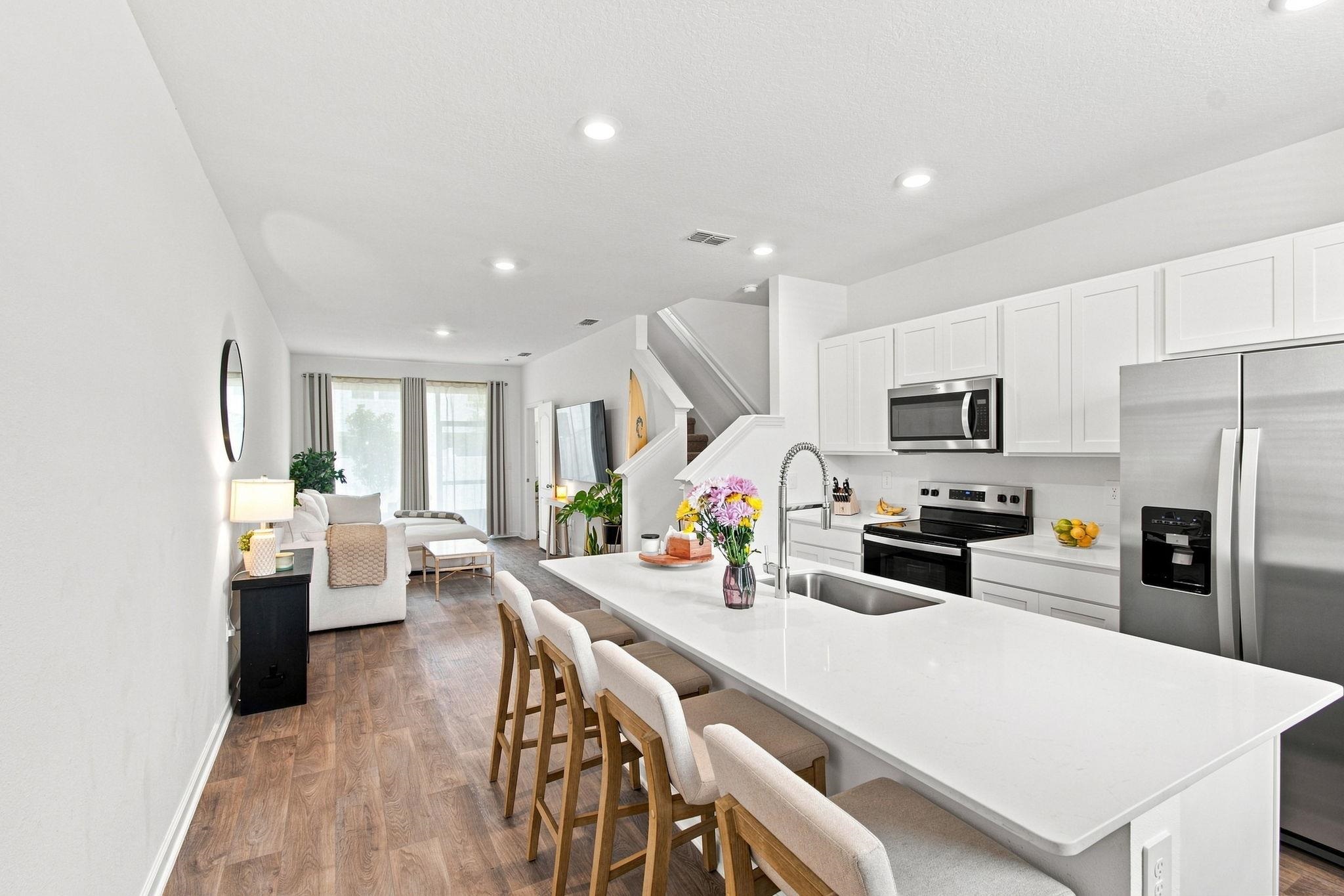 Open-concept kitchen featuring an expansive island with seating, stainless steel appliances, white cabinetry, and wood-finish flooring throughout Kitchen