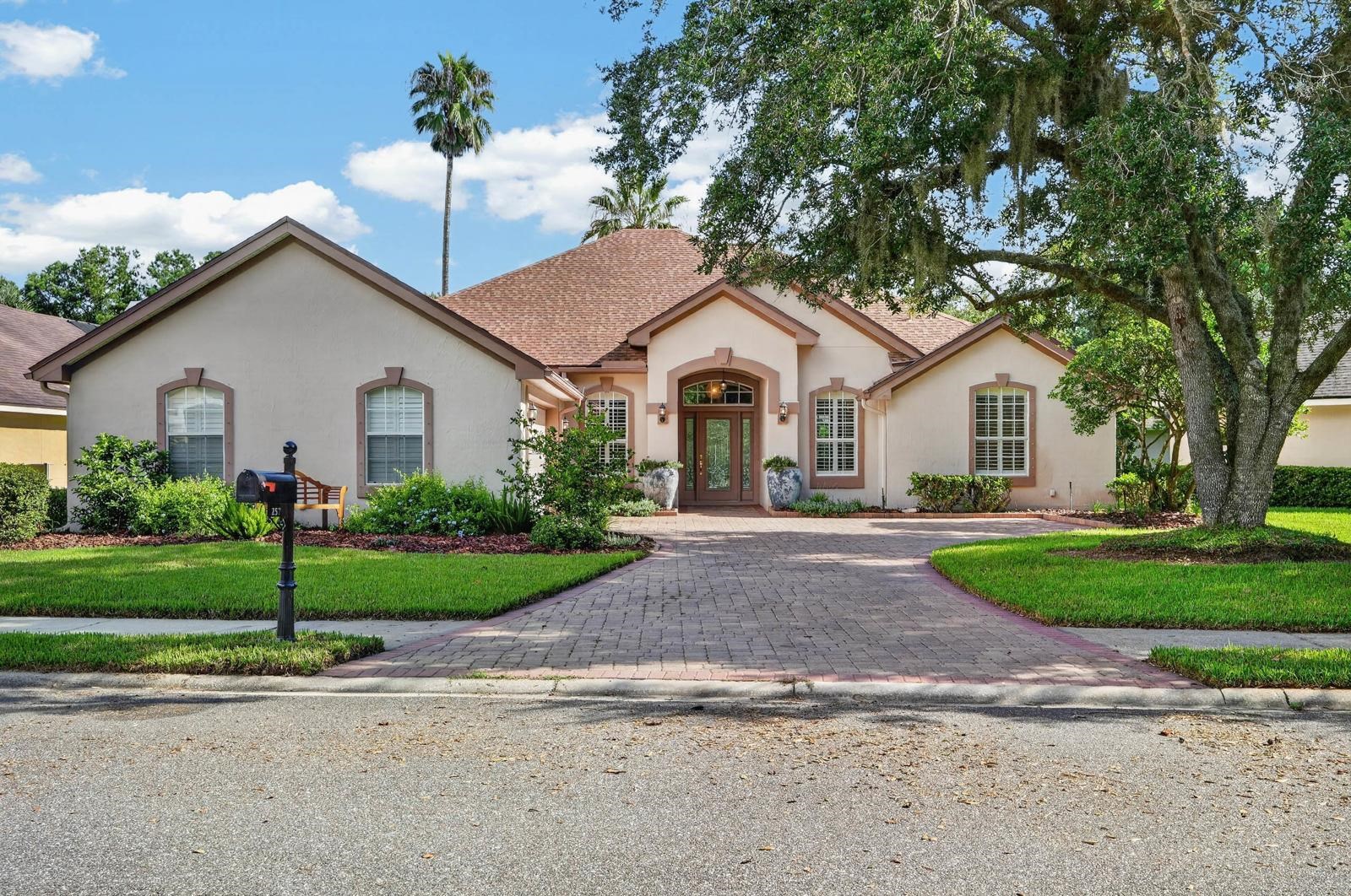 Stucco exterior with a hip roof, arched entryway, and a paver driveway Front Of Structure