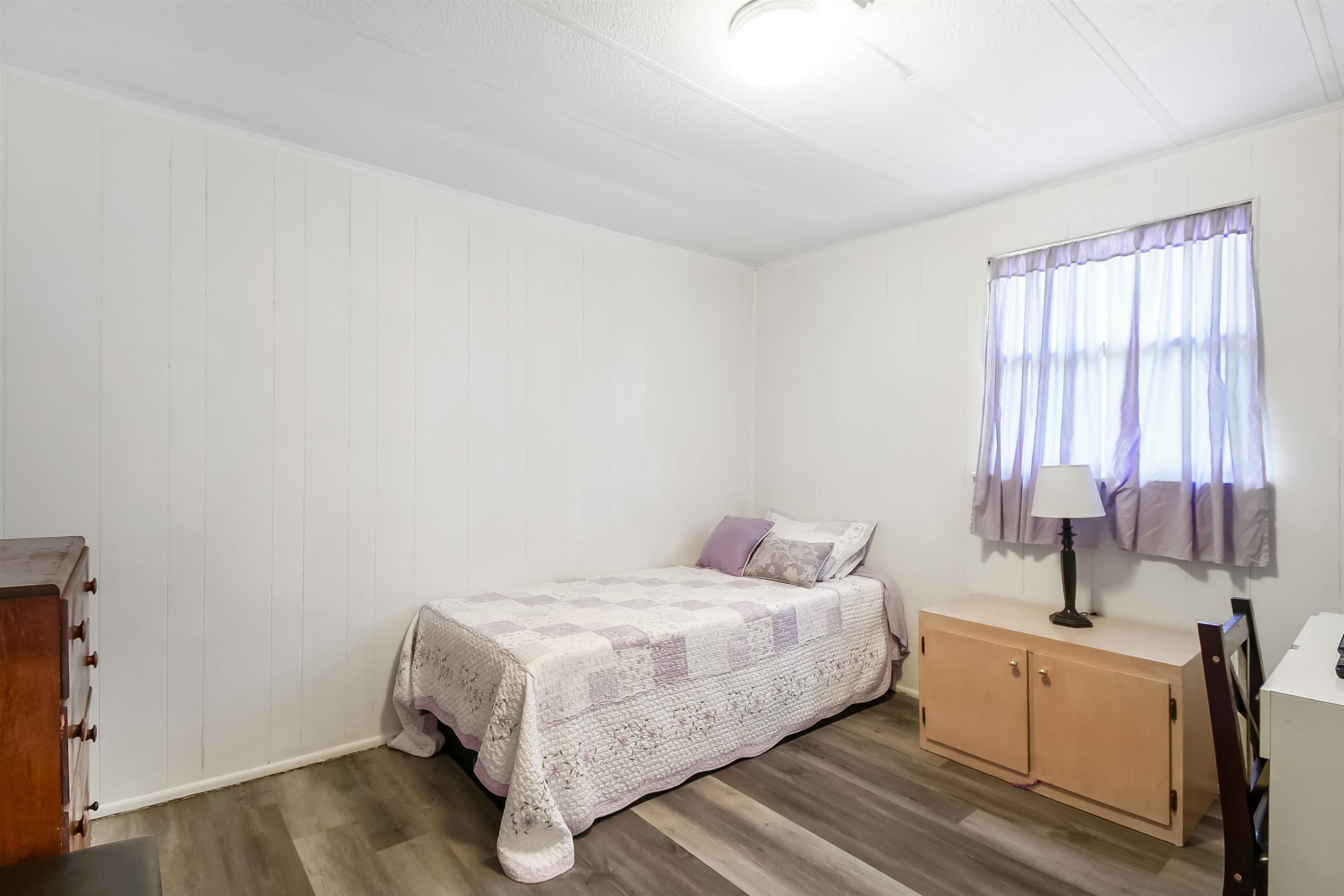 Wood-finish flooring with white vertical paneling and a ceiling-mounted light fixture Bedroom