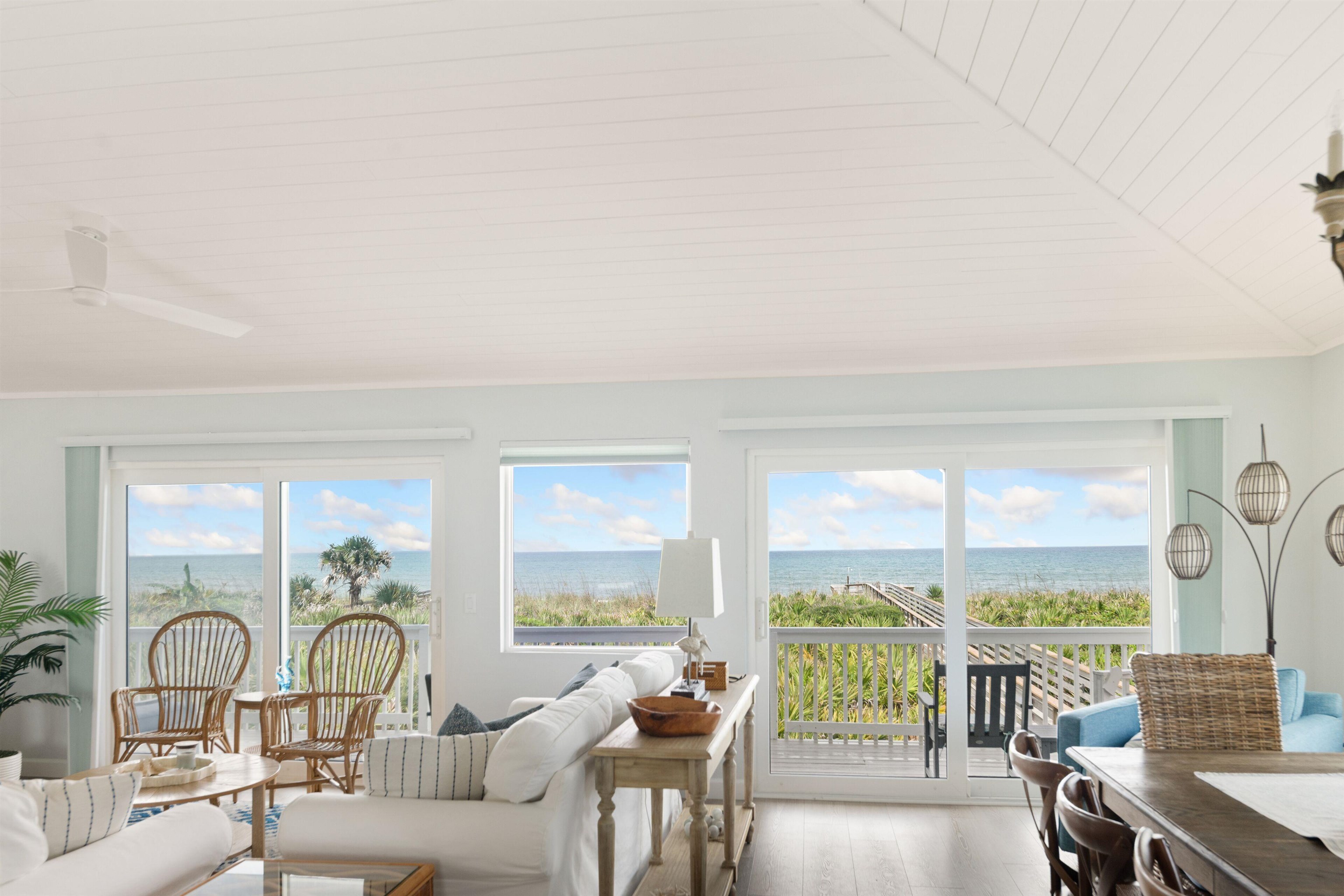 Furnished coastal living room with ocean views through broad windows and sliding doors, and a boardwalk outside.