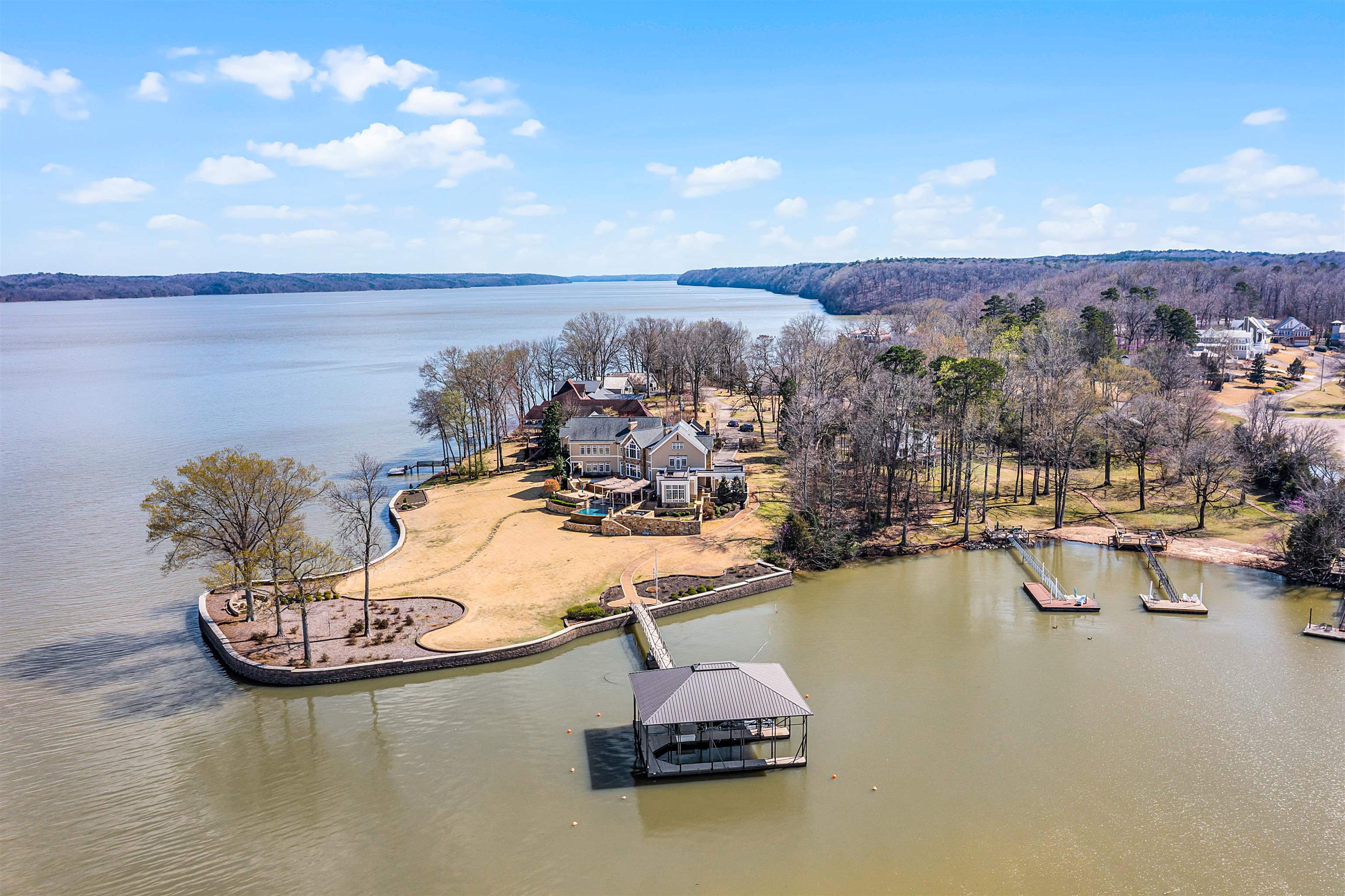 Aerial view of a waterfront home on a landscaped peninsula with docks and a covered boat slip.
