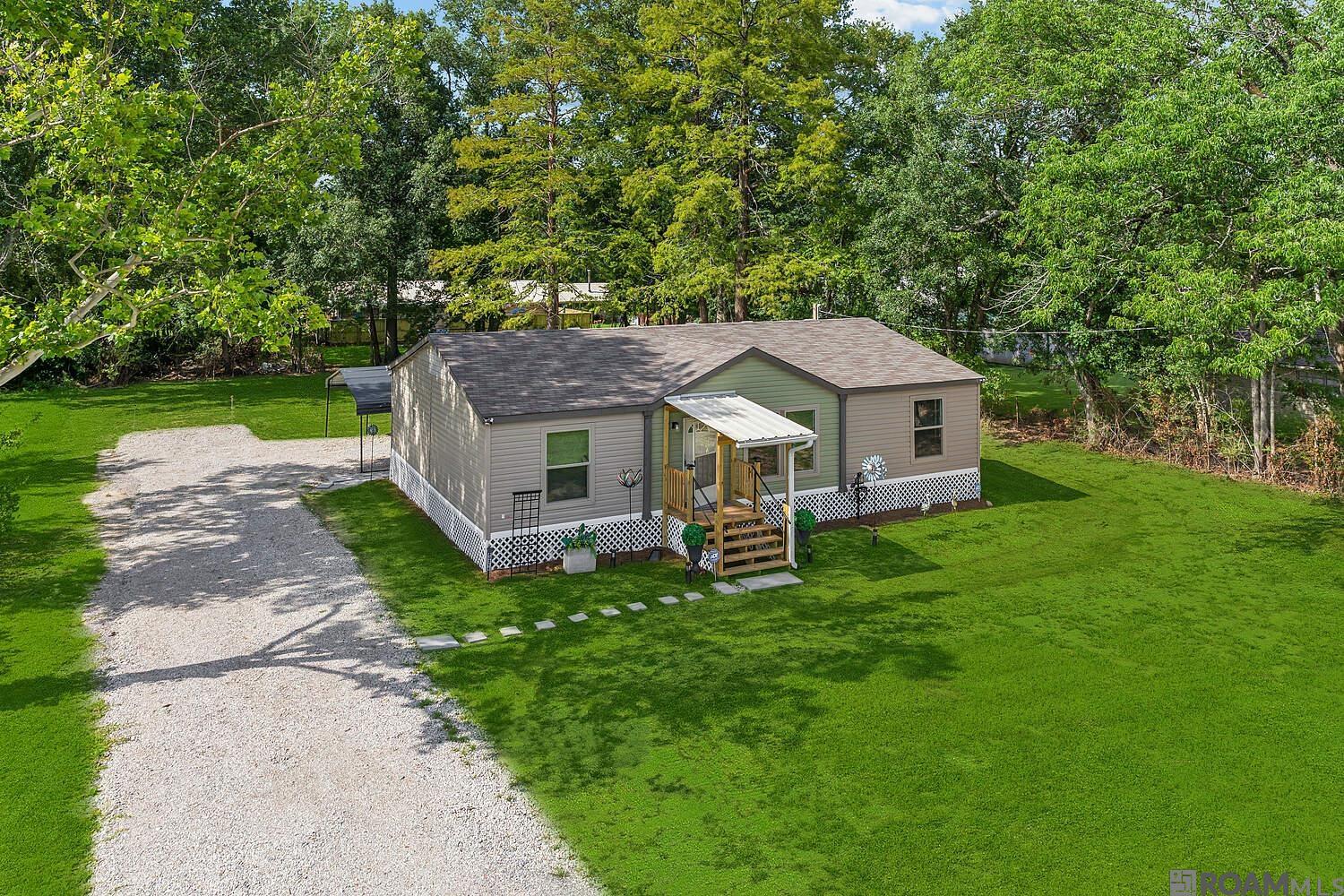 Gorgeous 2021 DW Mobile Hm -approx 1/2 Acre in Excellent Condition! Open Floor-plan w/ Upgrades: Stainless Appls w/ Refrigerator, Decorative Lighting & Mirror, AC Vents in Ceiling, Multi Trim Colors on front. New Fireplace: 53” Gray Faux Stacked Sandstone Infrared Quartz, Blk Faux Oak Top/Base + Remote! Steel front & rear Porch w/ Lights! Mature Trees, Dbl rear Carport + extra Parking & Patio Canopy-vented Double Roof. New: 100ft driveway, grade dirt on lot, installed new lift station & drain. Your Oasis to add: Pool, BBQ area & More to enjoy w/your Family & Friends! Close: Prairieville High School/Dining/Shopping/Movie Theatre/Library/ Walmart/ Pharmacy & 10 min's to I-10. No Flood Insurance! Welcome Home!