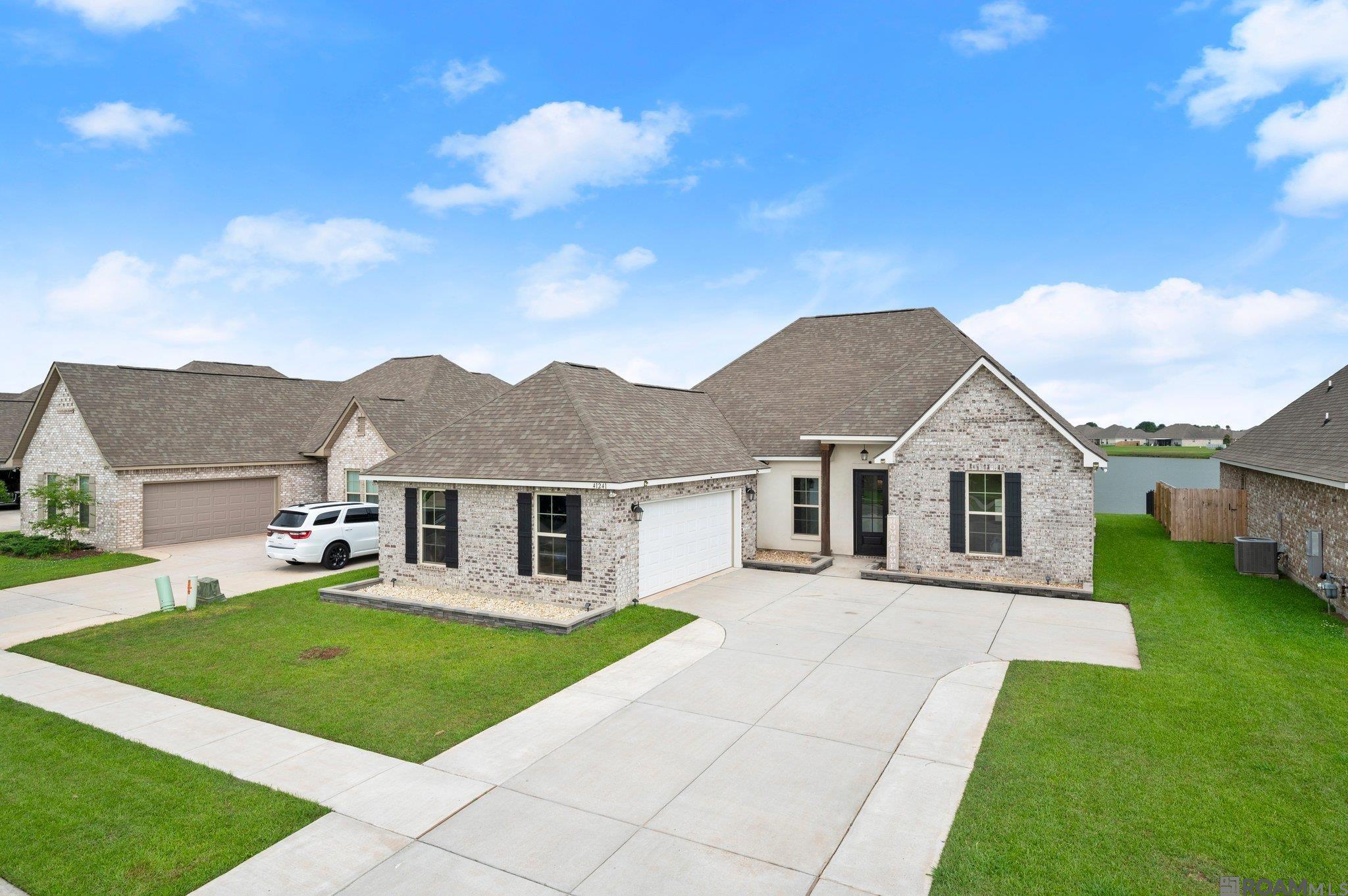 Better than new and loaded with upgrades, this 2022-built masterpiece offers one of the absolute best lake views in the sought-after Pelican Crossing community! This spacious five-bedroom, three-full-bath residence features a rare triple-split floor plan and luxury wood-look ceramic tile throughout—no carpet here! The soaring ceilings and upgraded LED lighting lead you into an expansive living area centered by a custom stone fireplace with a wood mantel and ventless gas logs. The chef’s kitchen is an entertainer's dream, complete with slab countertops, a custom tile backsplash, a large island with bar seating, and premium stainless steel appliances including a gas range. The primary suite serves as a private retreat, featuring tray ceilings and breathtaking views of the lake. The en-suite bath offers dual vanities, a garden tub, and a custom oversized tiled shower. Additional bedrooms are thoughtfully positioned for privacy, including a front guest room with custom wood accent walls and a shared bath with a custom tile surround. Beyond the interior, the home is packed with high-value functional upgrades including a tankless gas water heater, a post-tension slab, a widened driveway for ample parking, and a 50-AMP generator plug.  The outdoor space is equally impressive, boasting a fully fenced backyard with a covered porch and an extended concrete patio perfect for sunset views over the water. Located in Flood Zone X (no flood insurance required) near I-10, Pelican Crossing residents enjoy access to two community pools and prime convenience. Call for your private showing today!